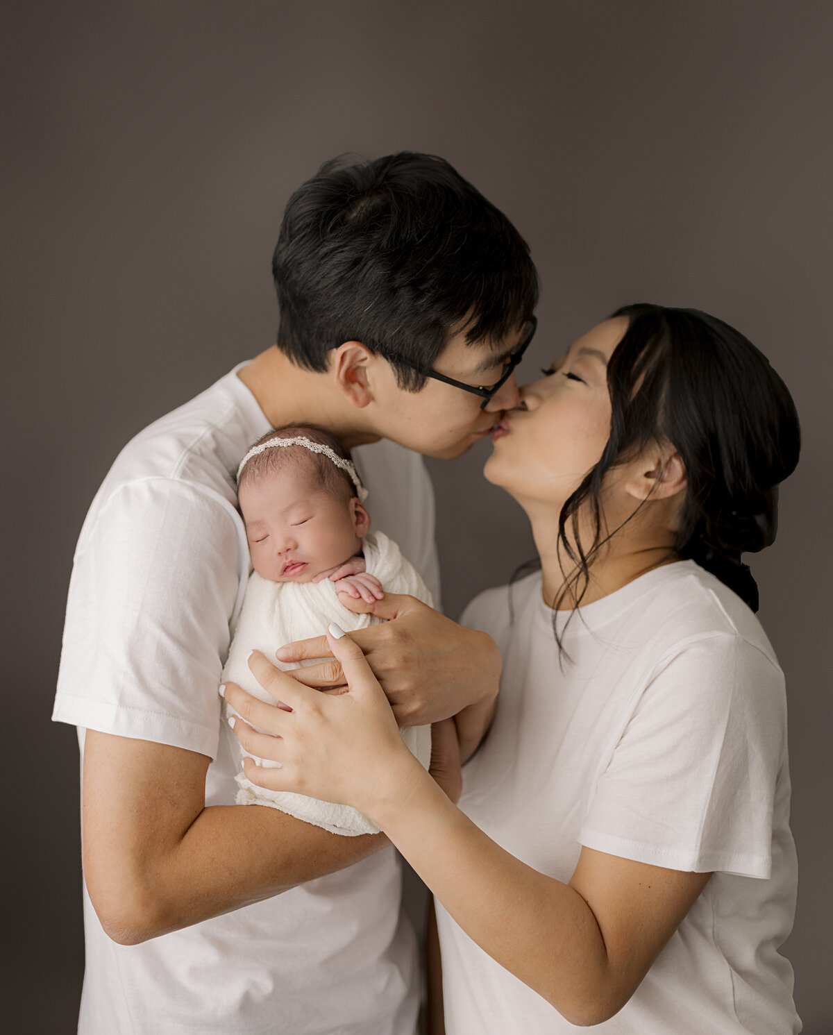 mom and dad kissing while holding newborn baby