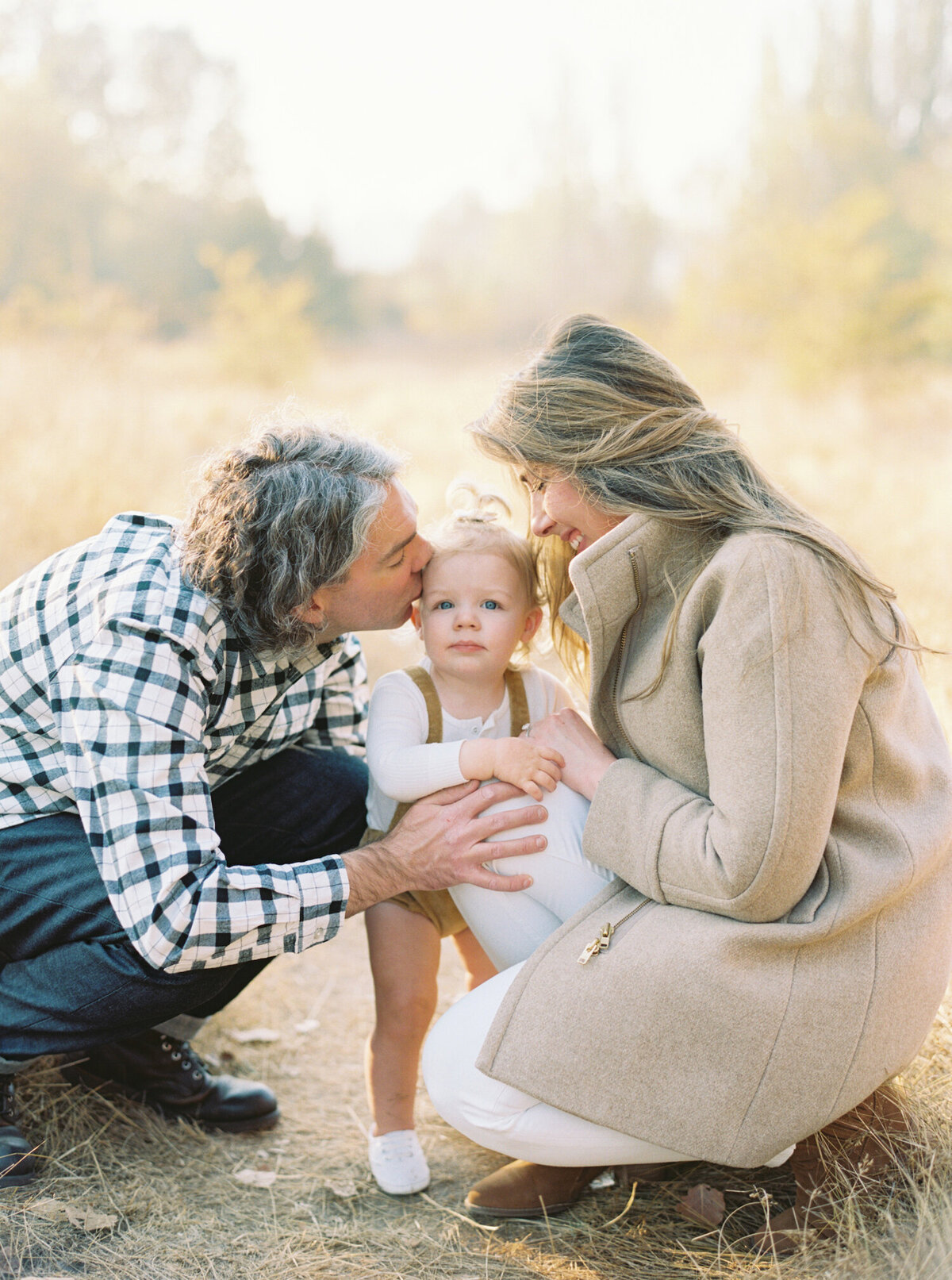 Fall Seattle Family photos of mom and dad kissing toddler girl as she stands on her own, with plaid and tan outfits. 