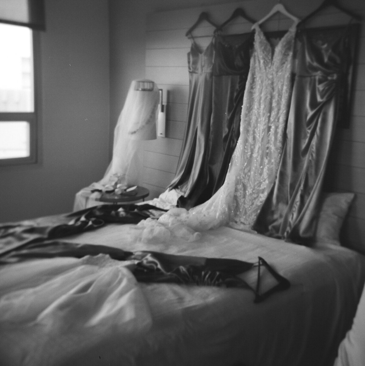 Bride and bridesmaids’ dresses neatly lined up on a bed in Carmel, CA, captured on film, showcasing wedding details — by Kate Winters Photography.