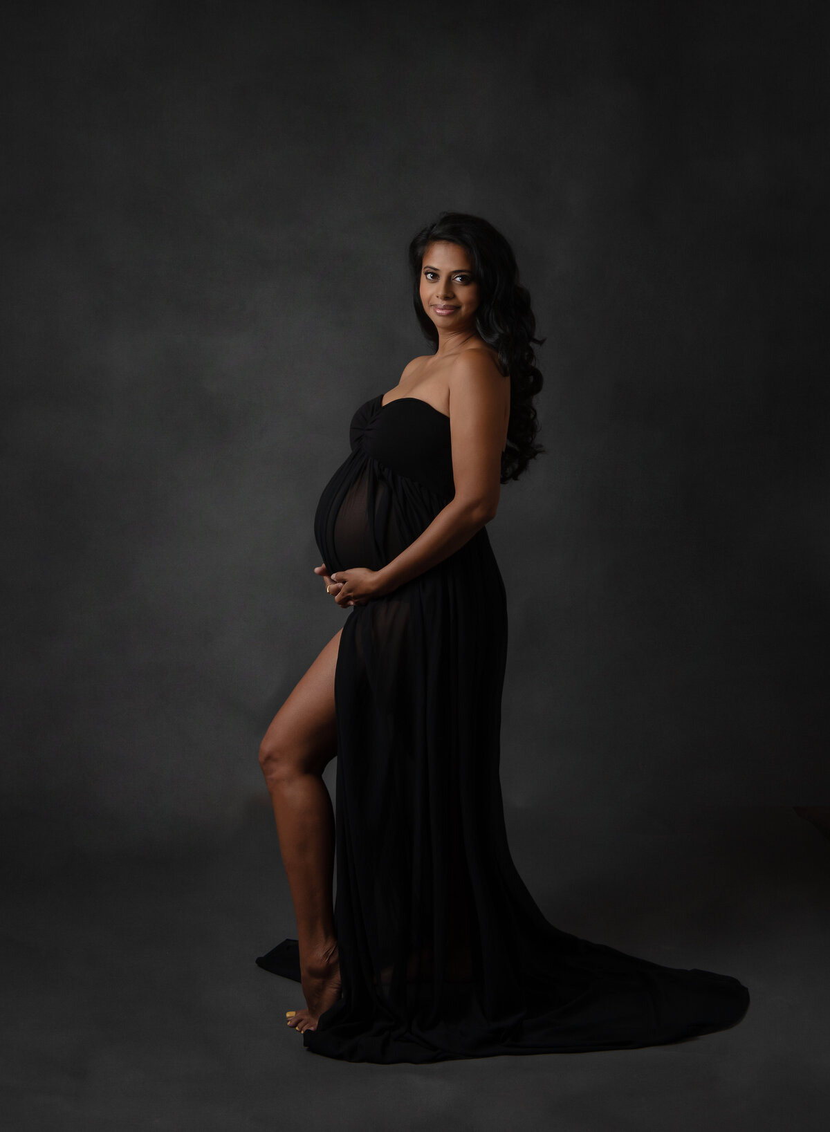 full length maternity portrait of woman on dark background in studio