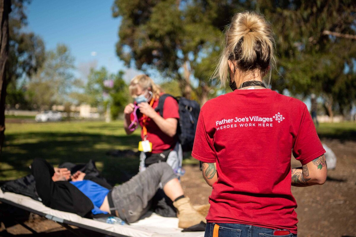 A homeless man is given assistance by Father Joes Street Health team in Balboa Park San Diego. Two field nurses speak with a sick man on a cot