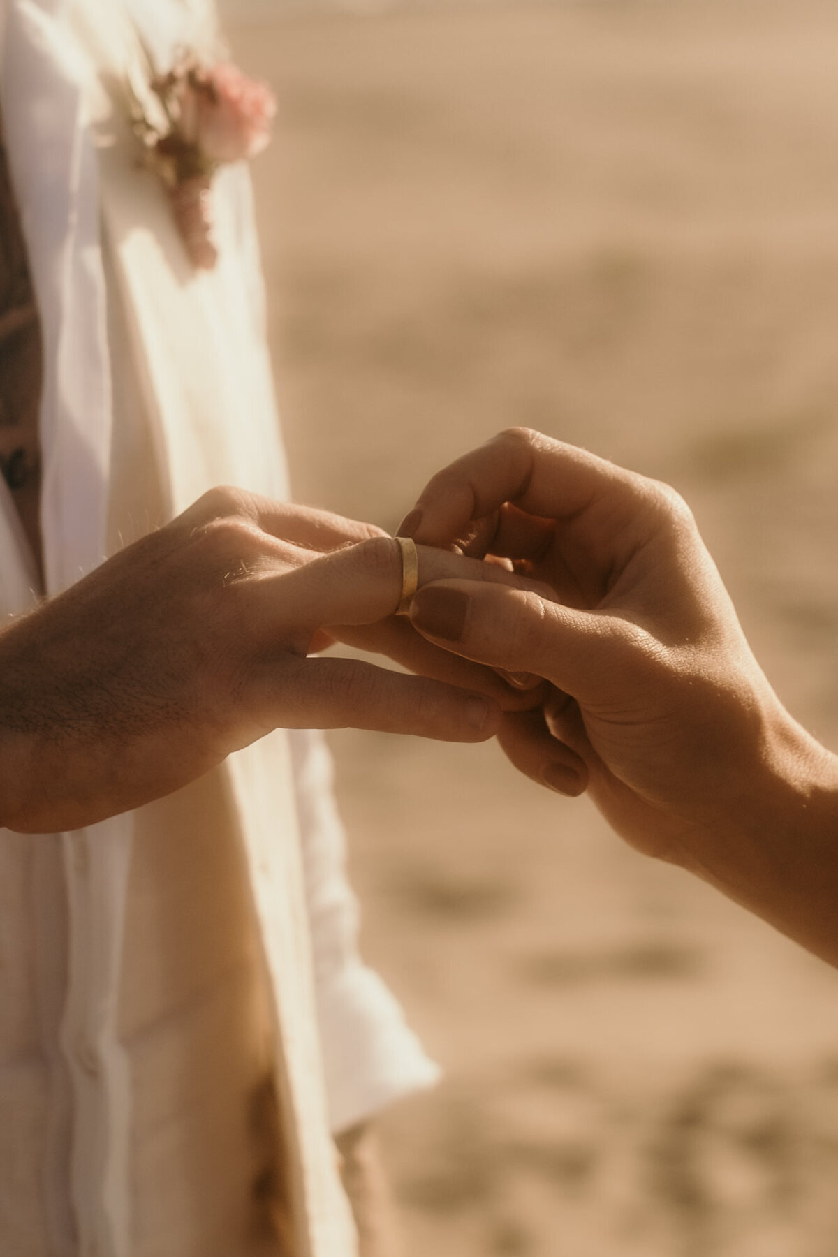 Mit einer Hand steckt die Braut ihrem Bräutigam den Ehering an den Ringfinger.