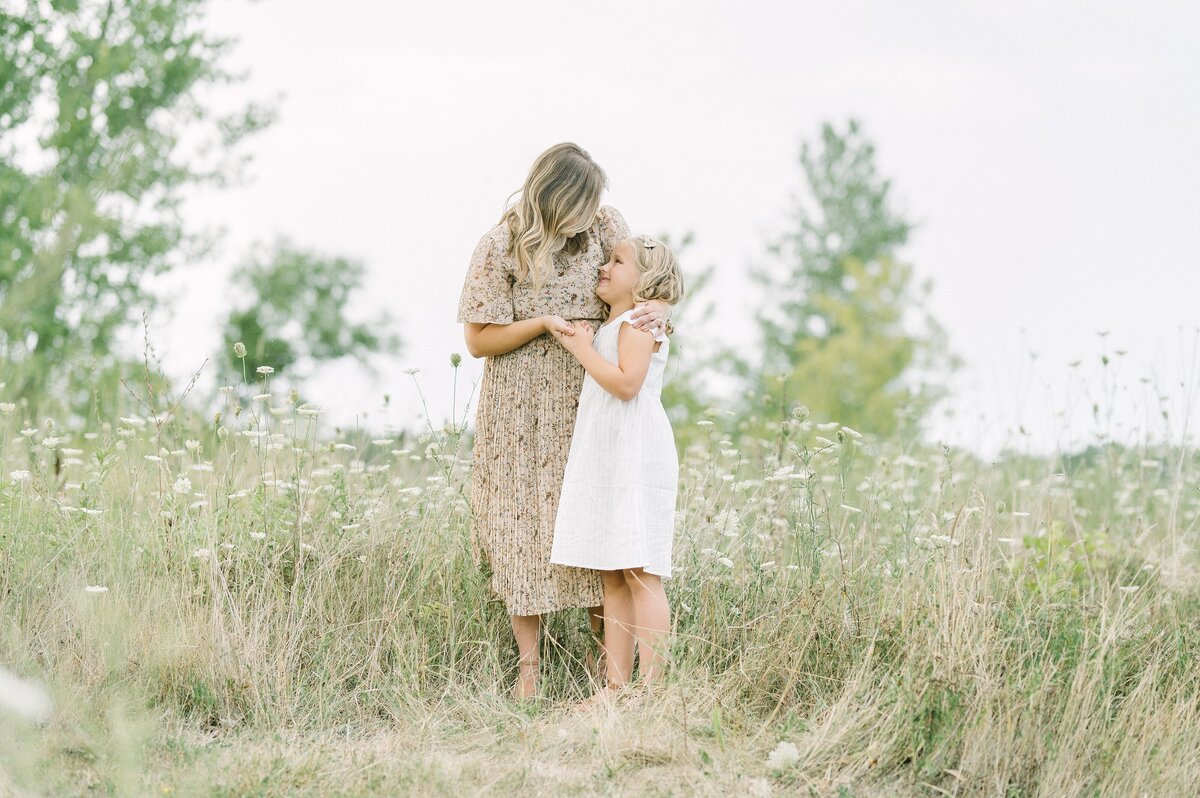 Pulled back photo of mom hugging her 8 year old daughter in a grassy field