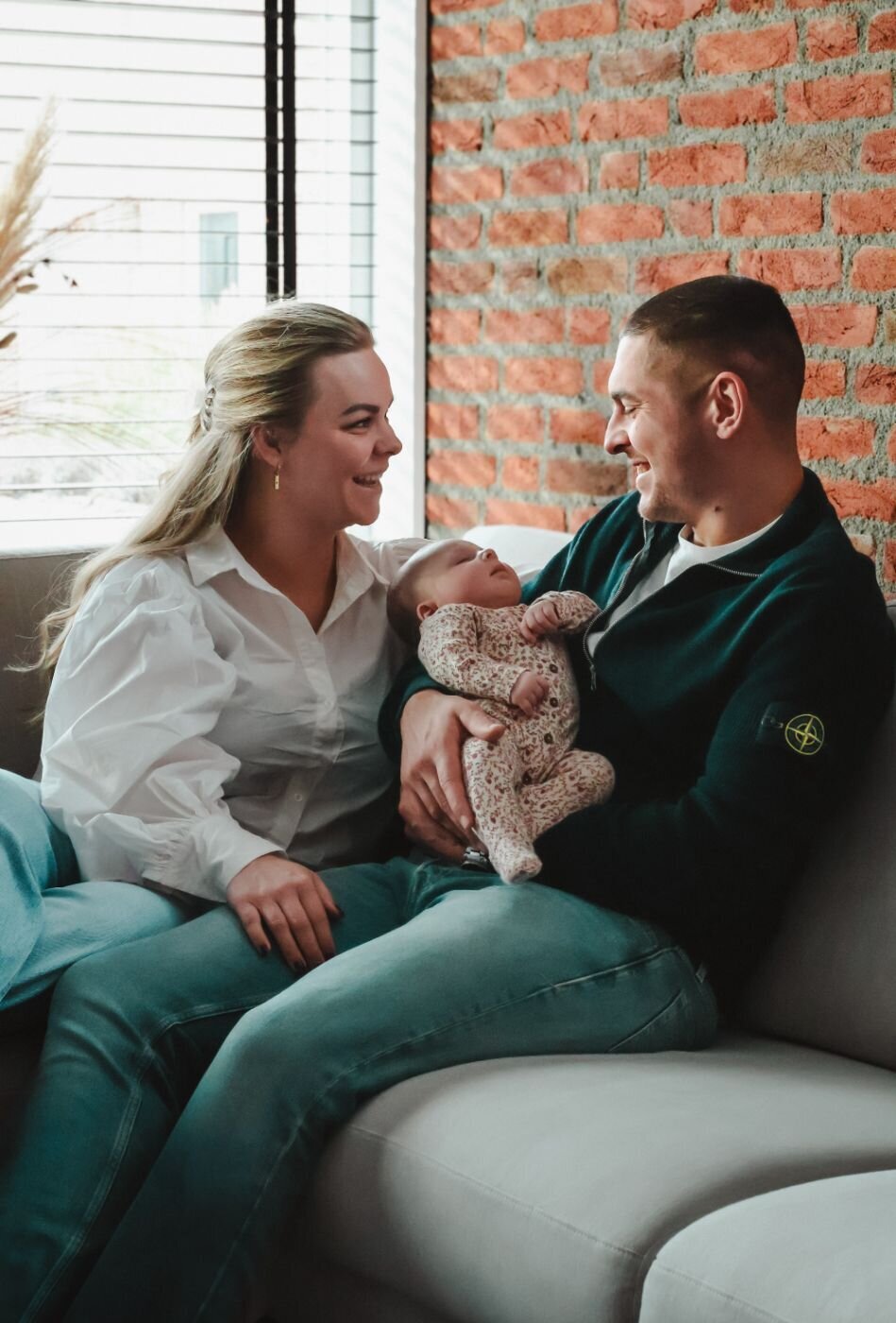 Een vader en moeder kijken liefdevol naar hun pasgeboren baby, terwijl ze samen op een bank zitten