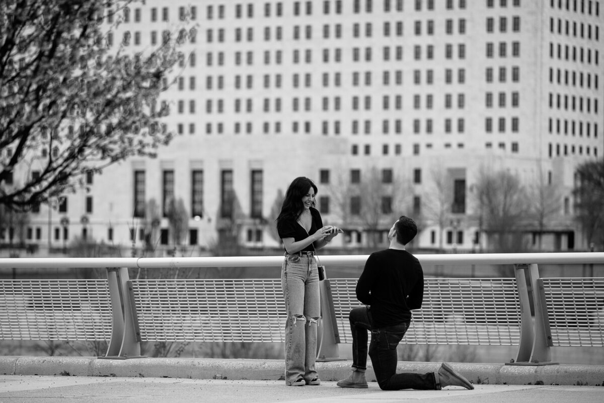 Man bends down on one knee and proposes to his longtime girlfriend in front of the Columbus skyline