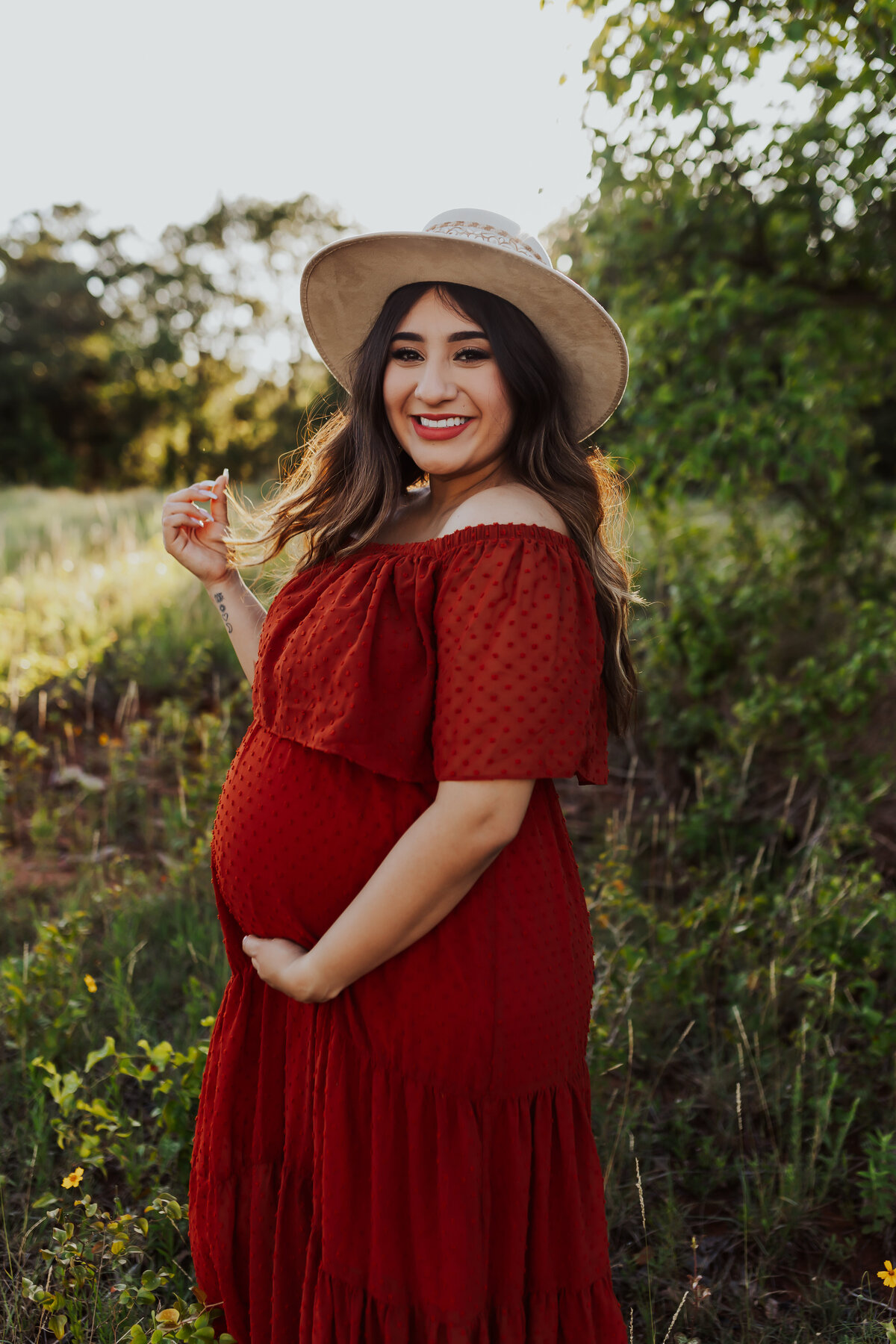 pregnant mother holding her belly bump wearing a red off the shoulder dress