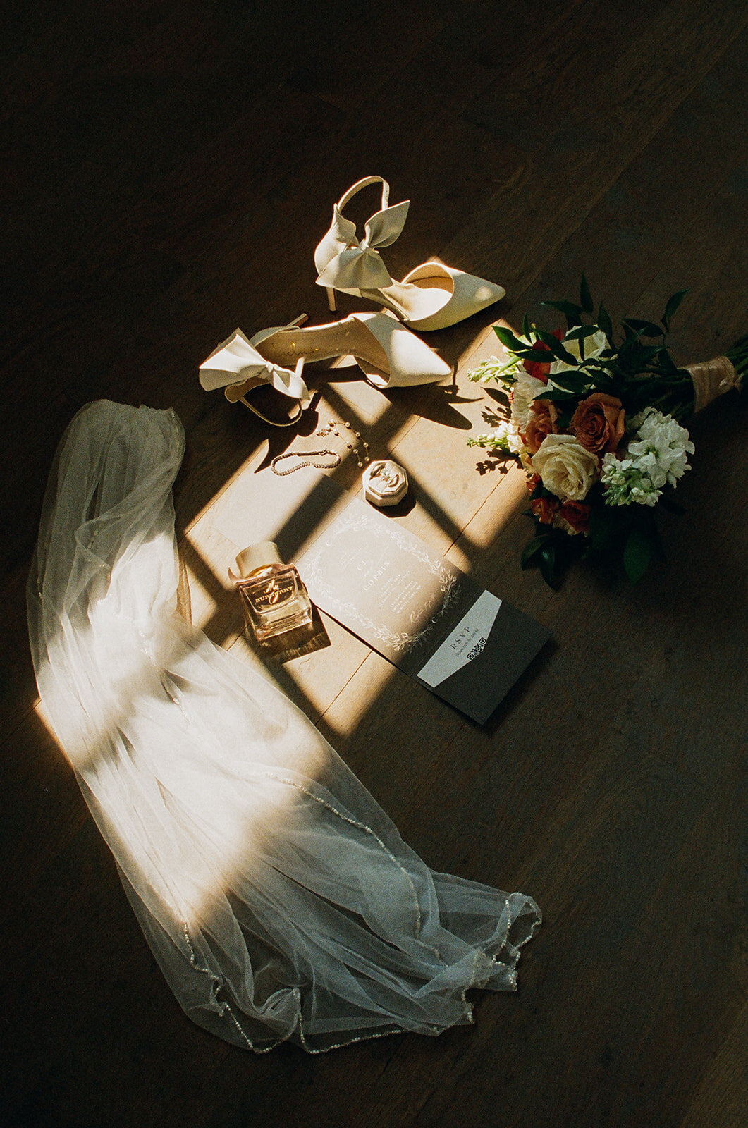 detail photo of wedding items like veil, shows, rings, invitation in a sunlit path from the window