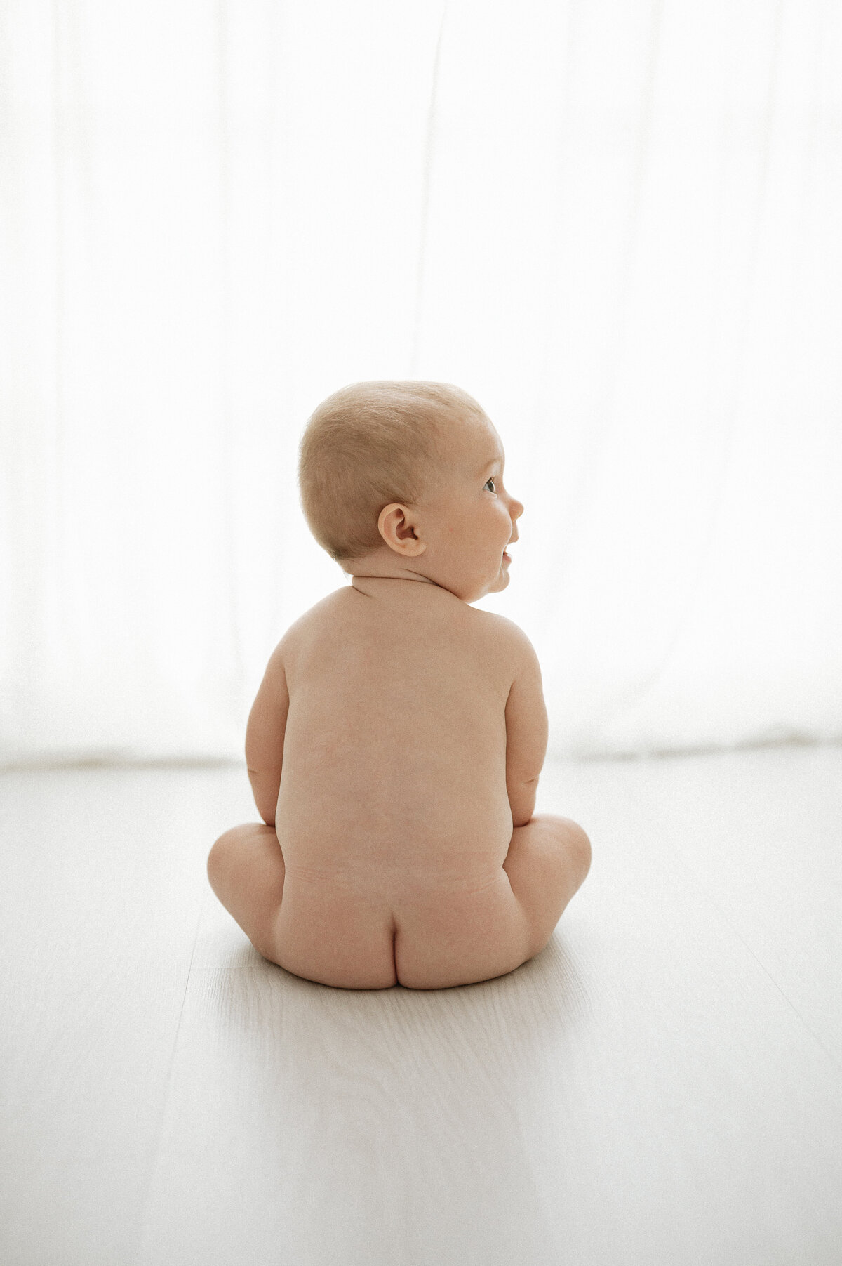 Naked baby sits looking out the window
