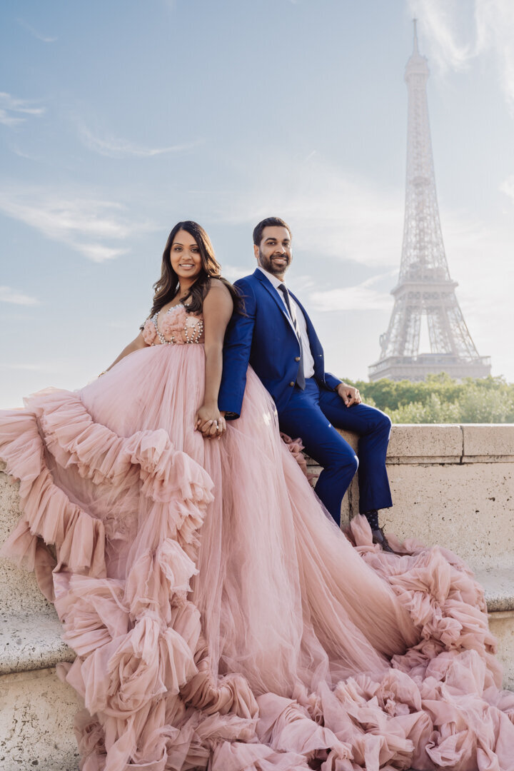 Romantic couple holding hands on wall, pink princess dress, Eiffel Tower view Paris