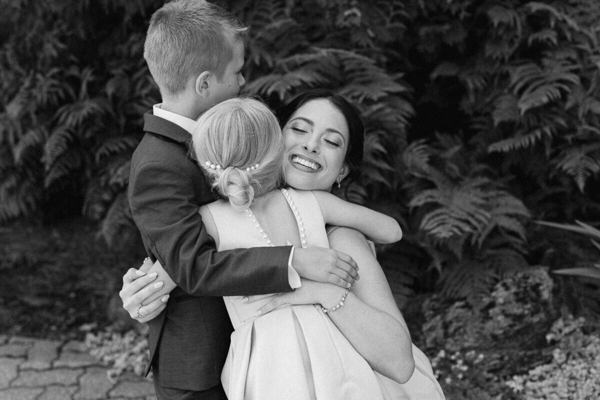 Deux soeurs et un frère se font un gros câlin lors du mariage de leur parents. 