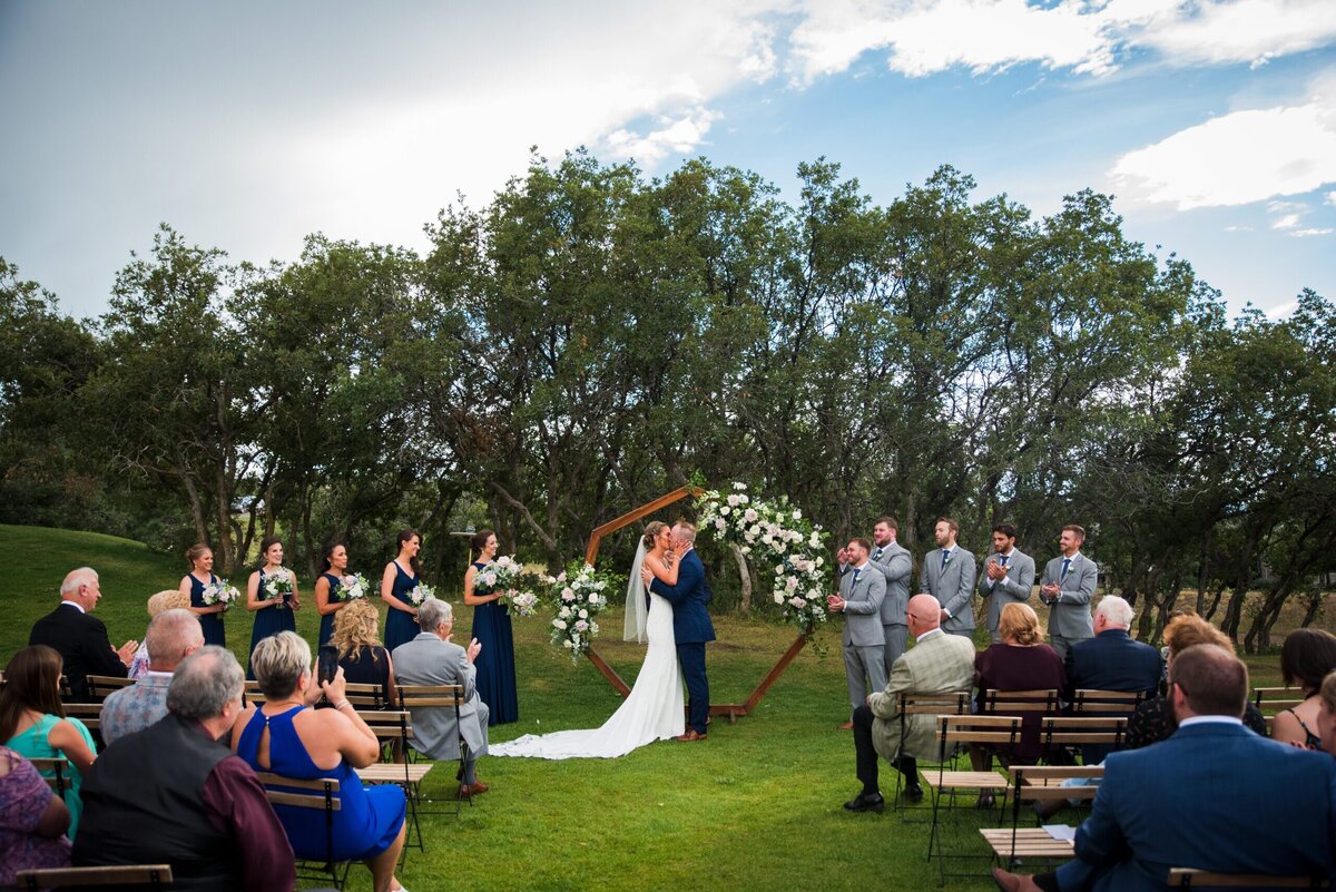 A wide angle shot of the bride and groom sharing their first kiss as the guests cheer.