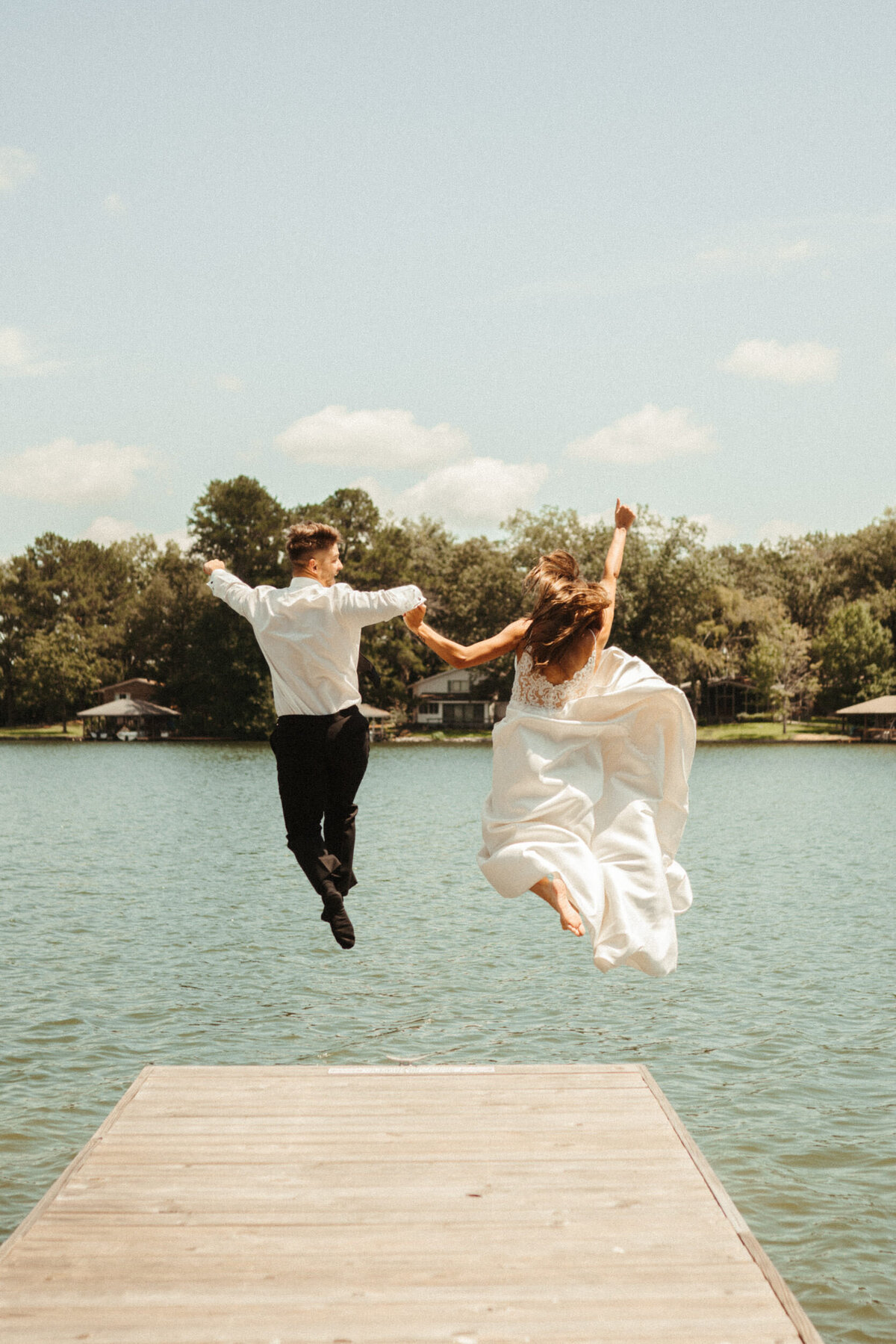 Bride and groom running down a pier and jumping into a lake in their wedding clothes