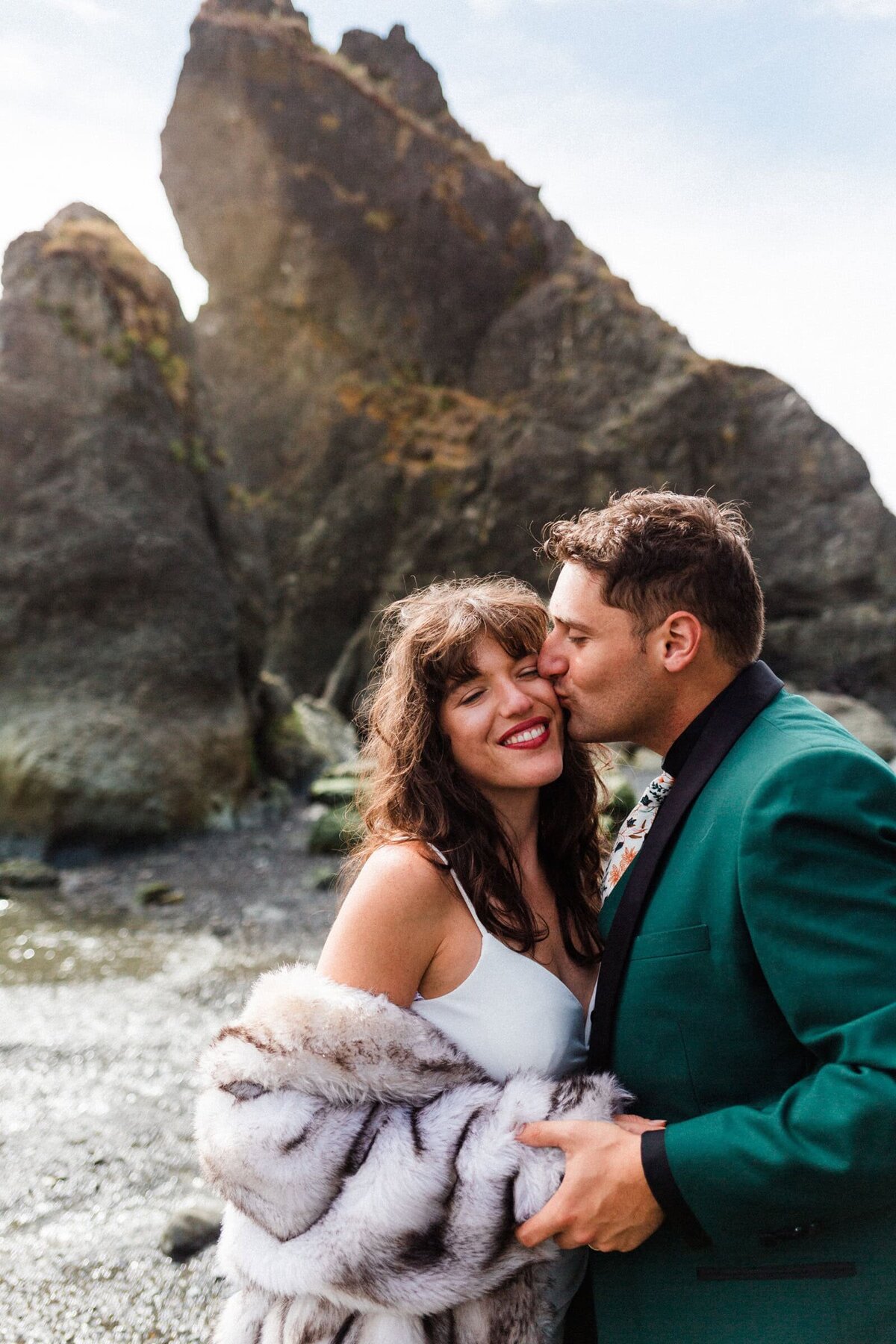 groom kissing bride on the cheek on Ruby Beach with sunrays