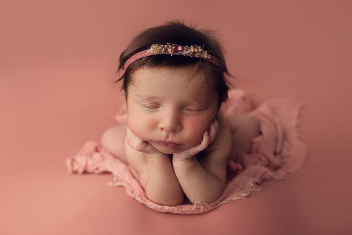 beautiful dark haired baby on a pink backdrop in froggy pose