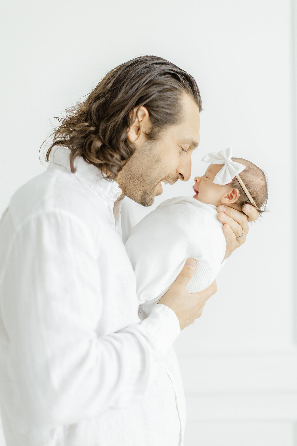 Close up side profile of a father standing in a DFW photography studio holding his newborn baby girl up as they both smile.