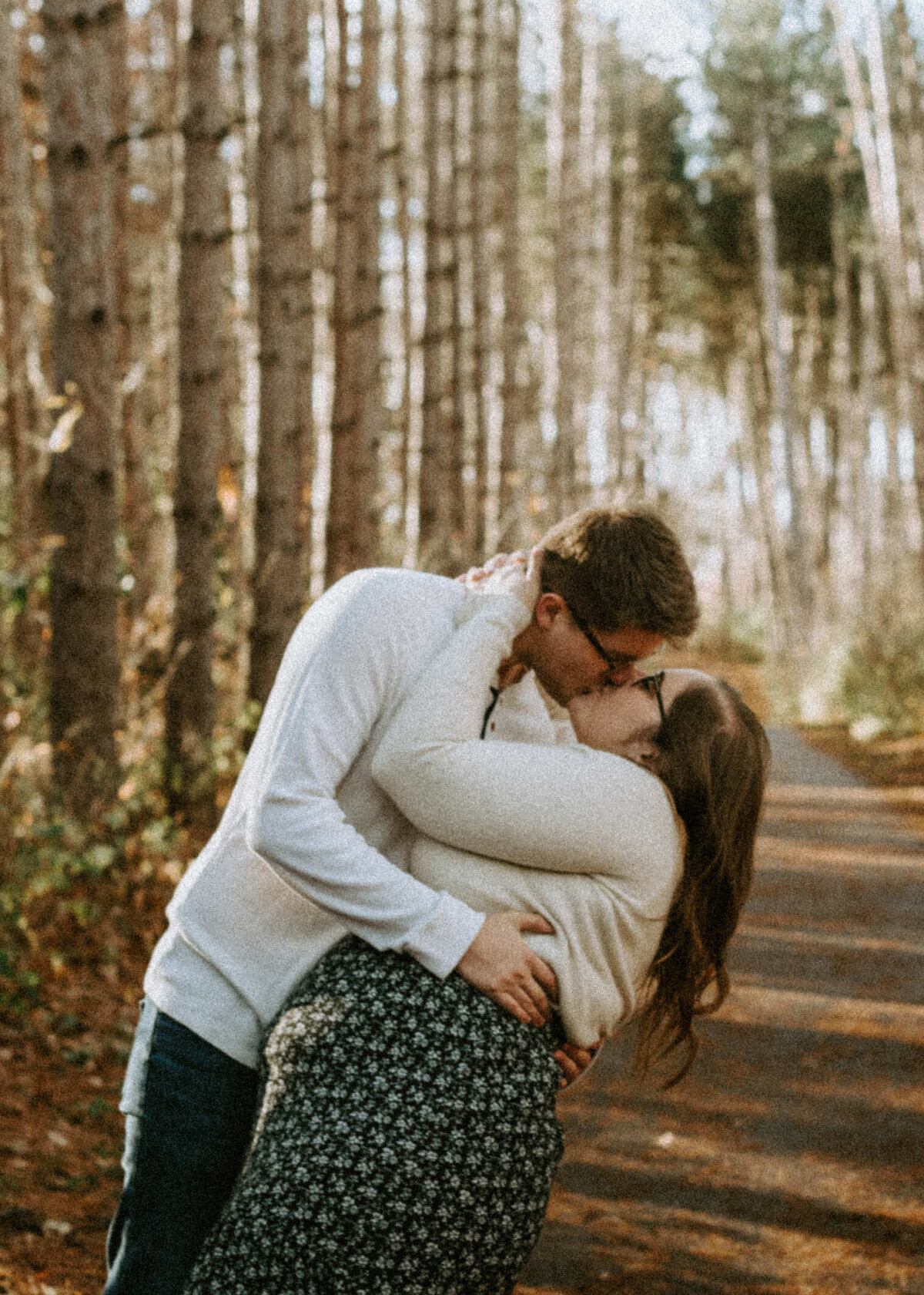 Couple kissing in a forest of pine trees.
