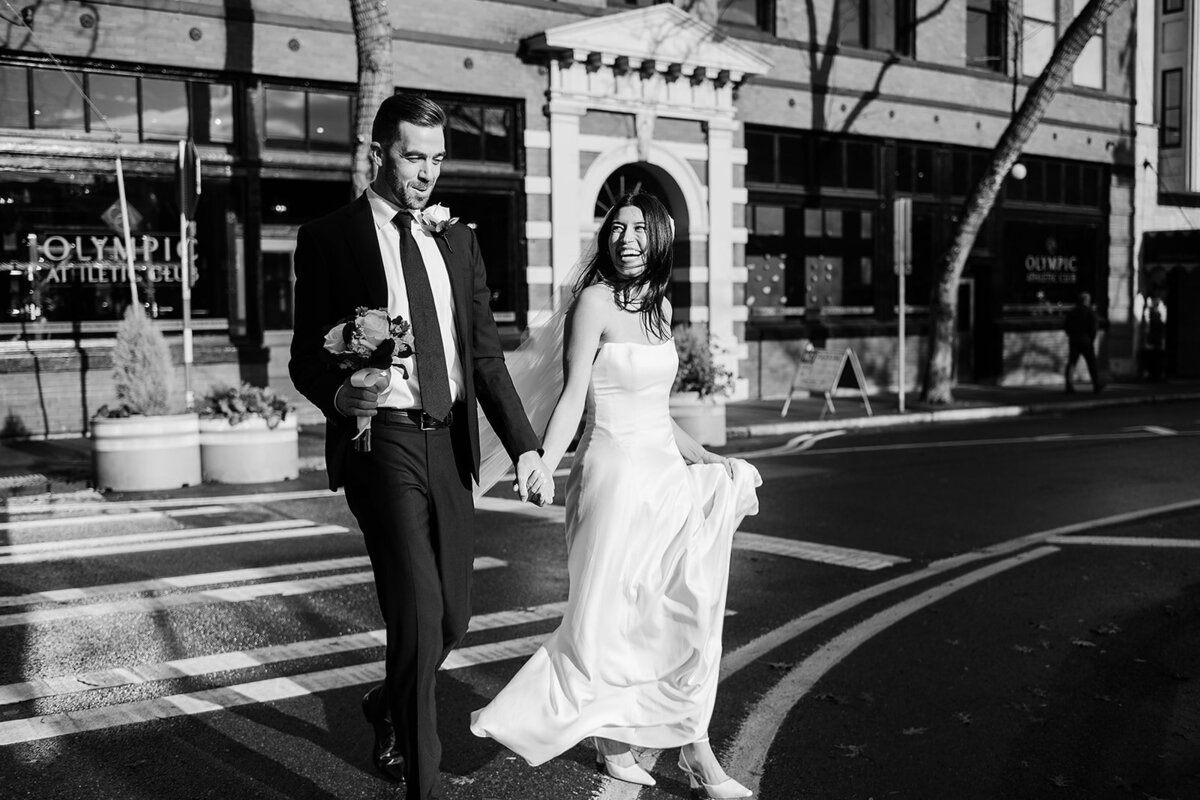Joyful couple walking hand in hand across the streets of downtown Ballard before their intimate micro wedding at the Ballard Locks Botanical Garden