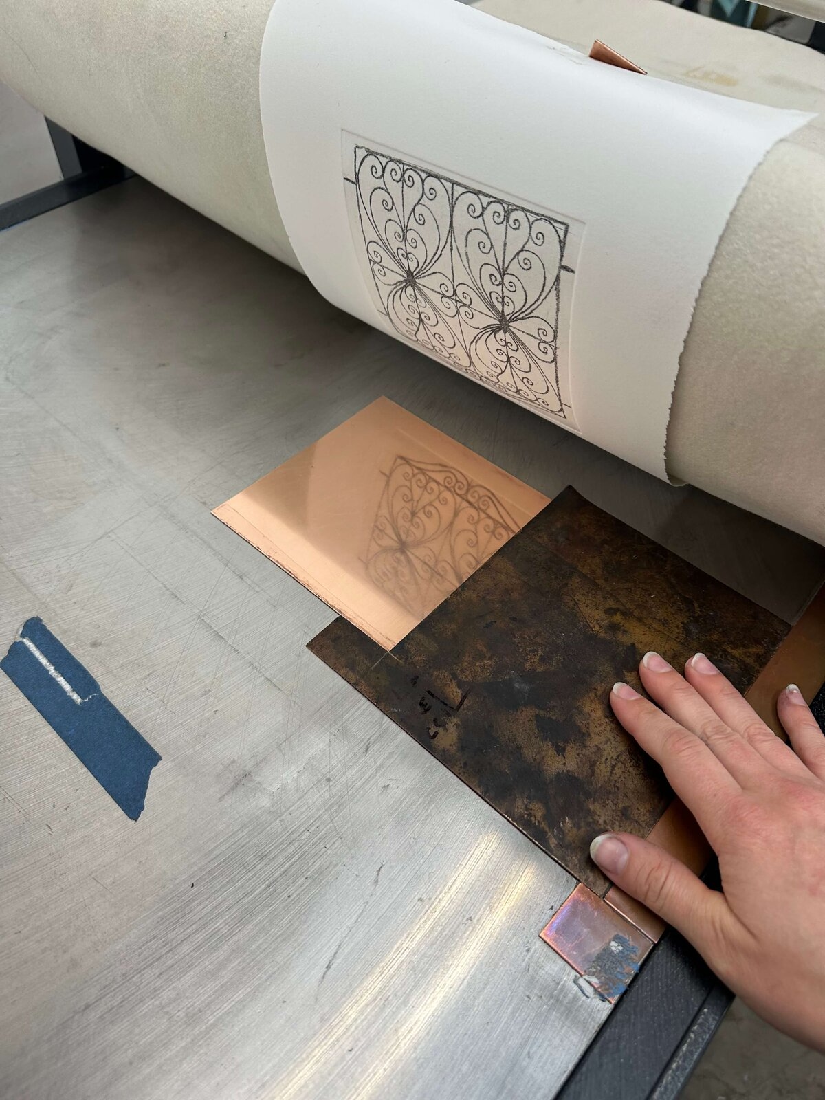 Paper being pulled from an etched copper plate on the press bed, showcasing the moment of reveal in line reversal printing.