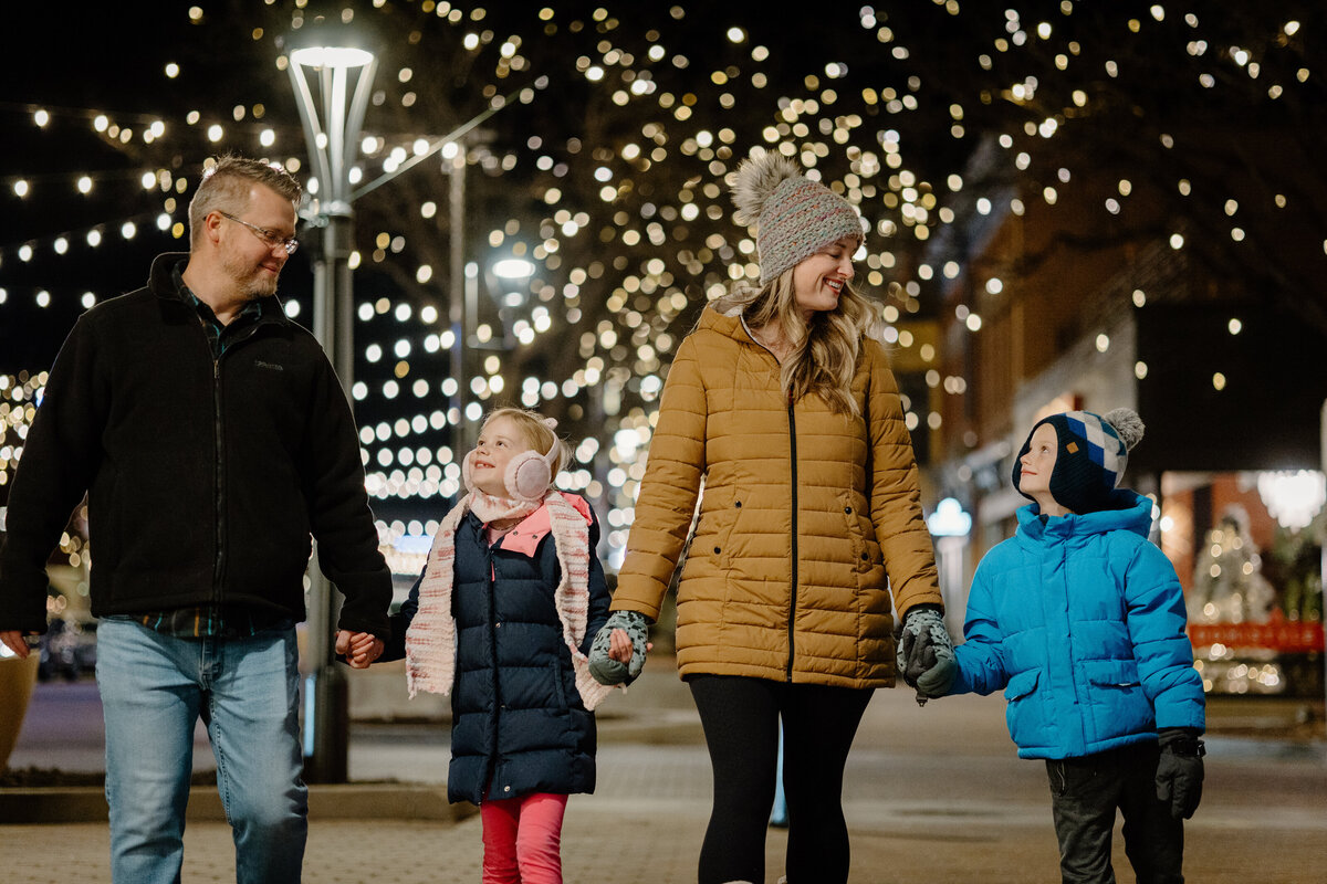 A family holds hands while walking through Old Town Fort Collins at night.