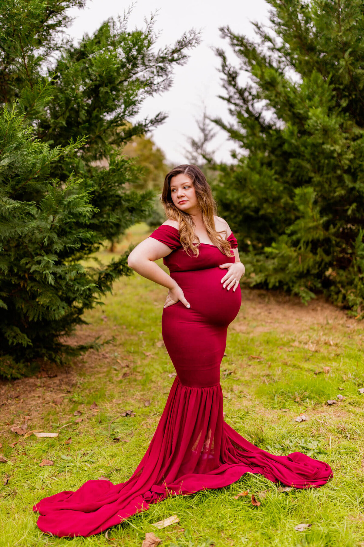 Pregnant mom in a maroon dress standing with some trees