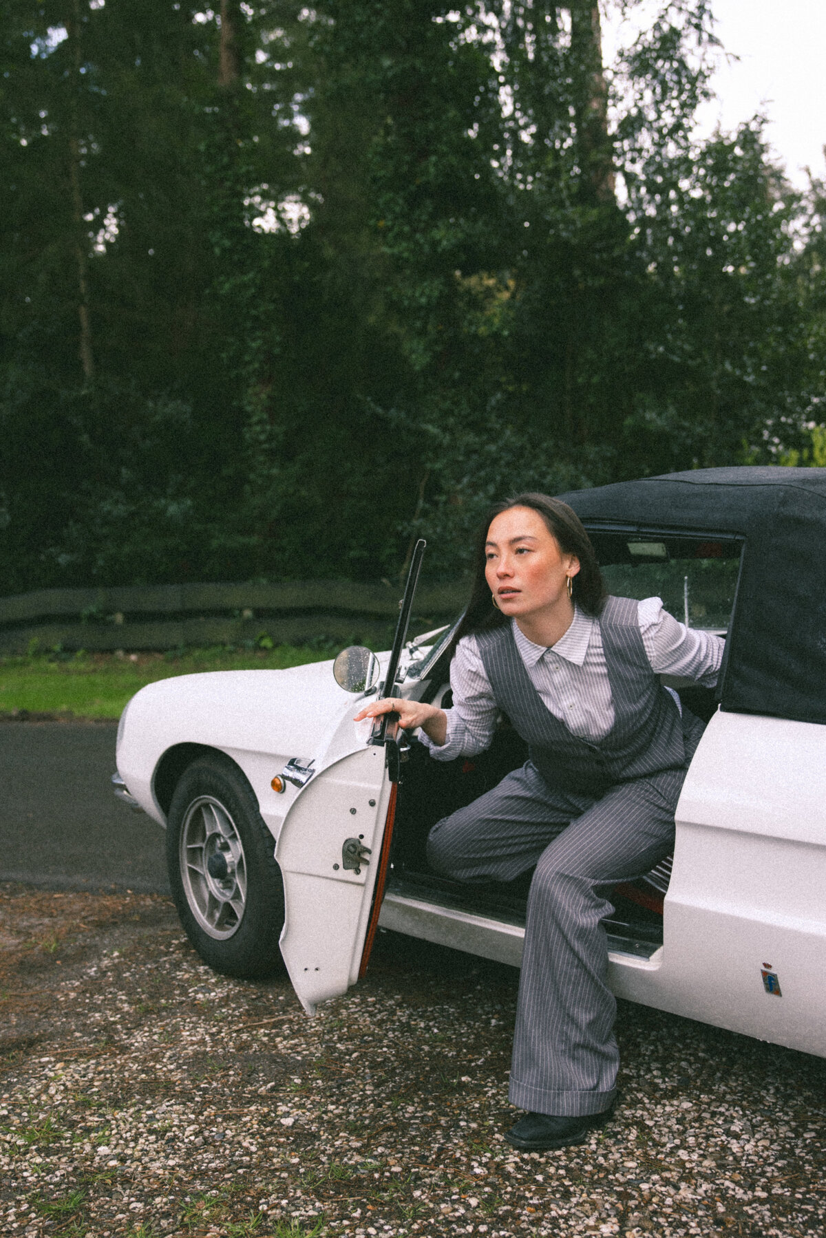 Stepping out of the car, the model exudes a sense of determination and poise. The forest setting adds a touch of mystery and depth, while her outfit choices keep the focus on her confident demeanor. Photographed by Bo Eppink.