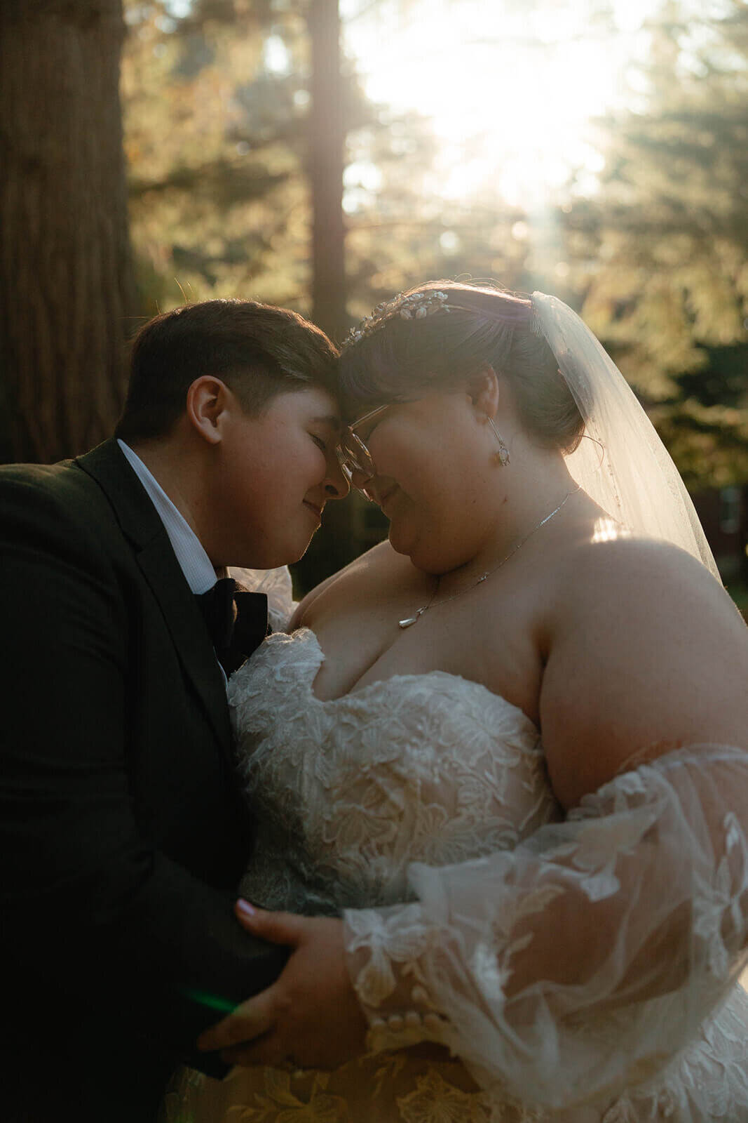A wedding couple embraces and places their heads together at their outdoor wedding ceremony.
