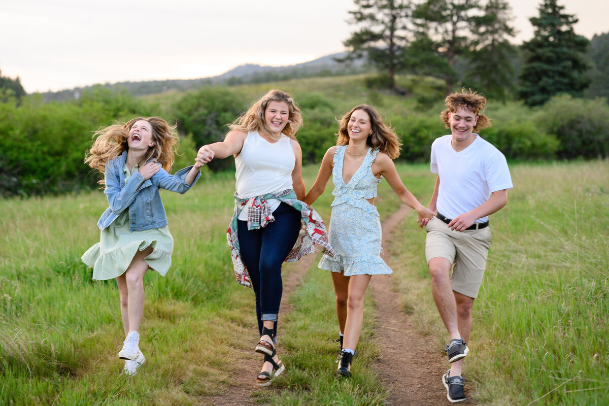 4 seniors skipping and laughing in a green mountain meadow at a rep team senior session by a denver senior photographer