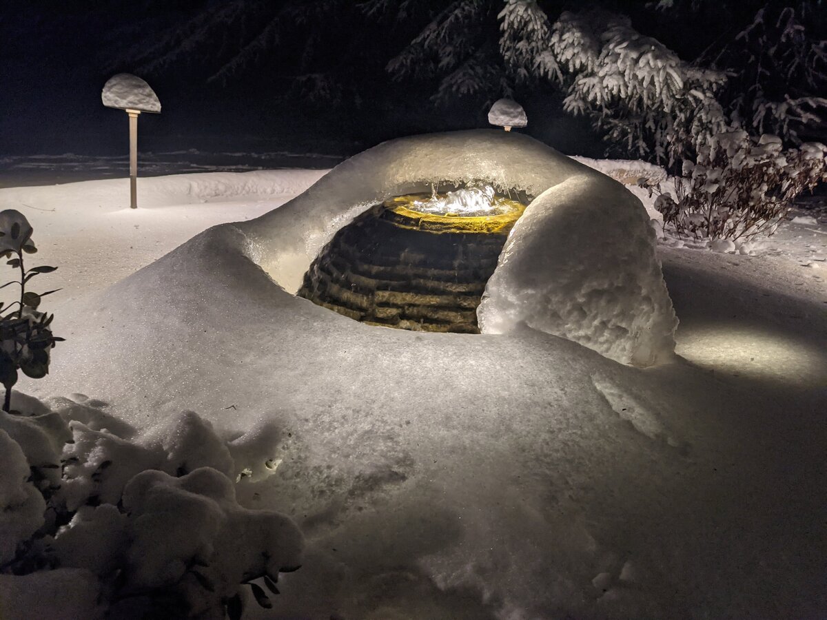 Backyard water fountain wrapped in a blanket of snow and lit up at night