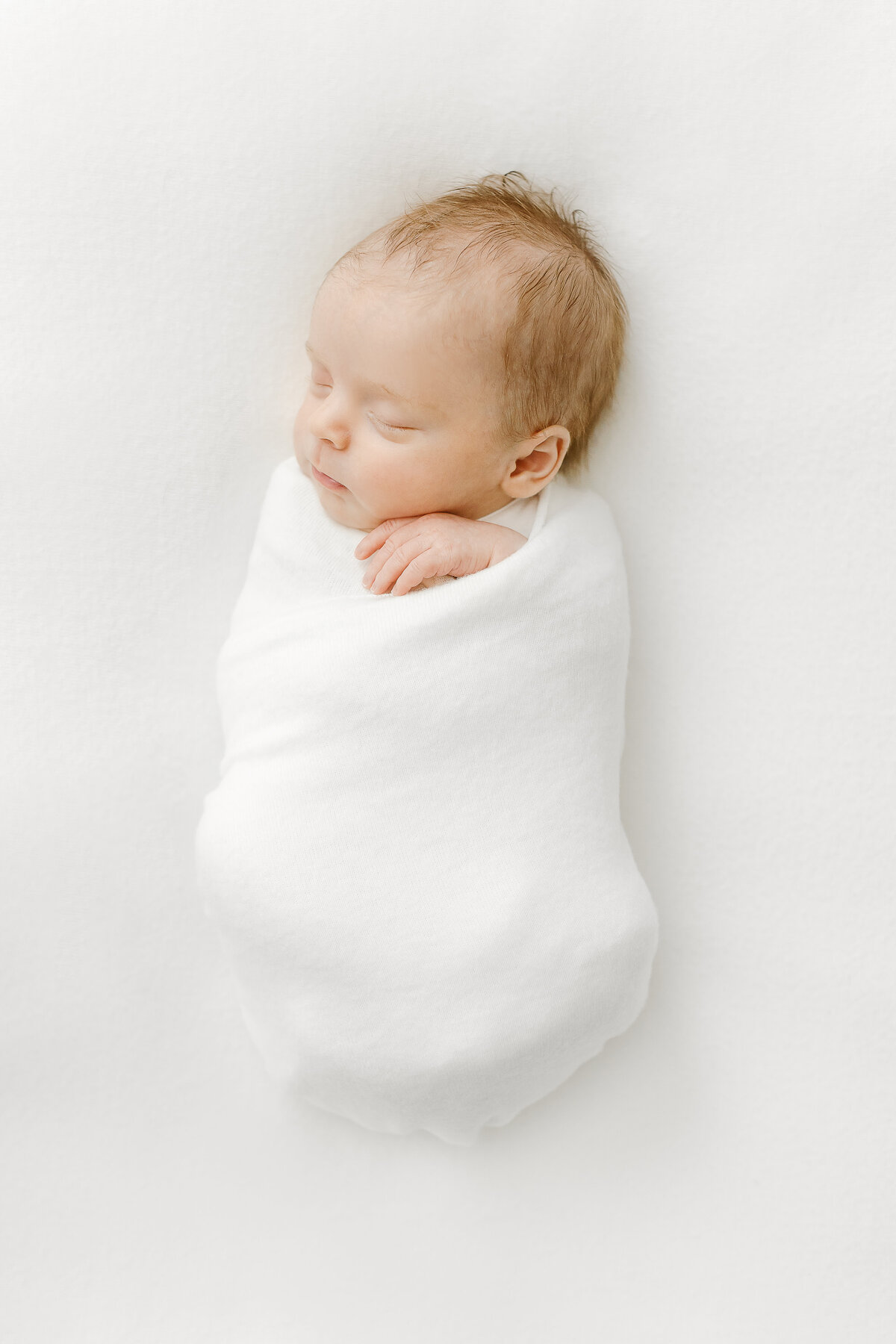 A Northern VA Newborn Photography photo of a beautiful newborn baby girl sleeping in a white swaddle blanket
