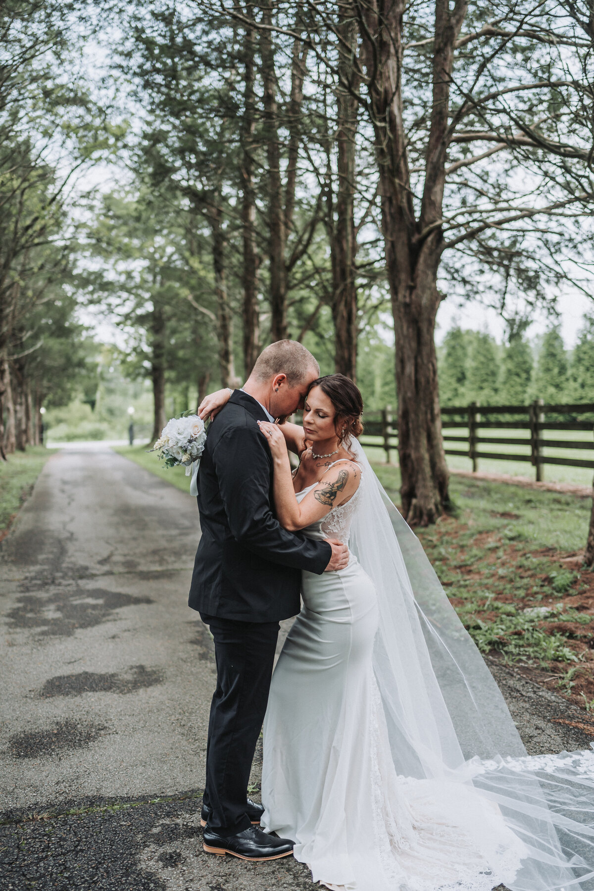 A newlywed couple shares a tender embrace under a canopy of tall trees at Gentry Farm in Danville, Virginia, capturing an intimate and romantic moment by Quinn Photography LLC.