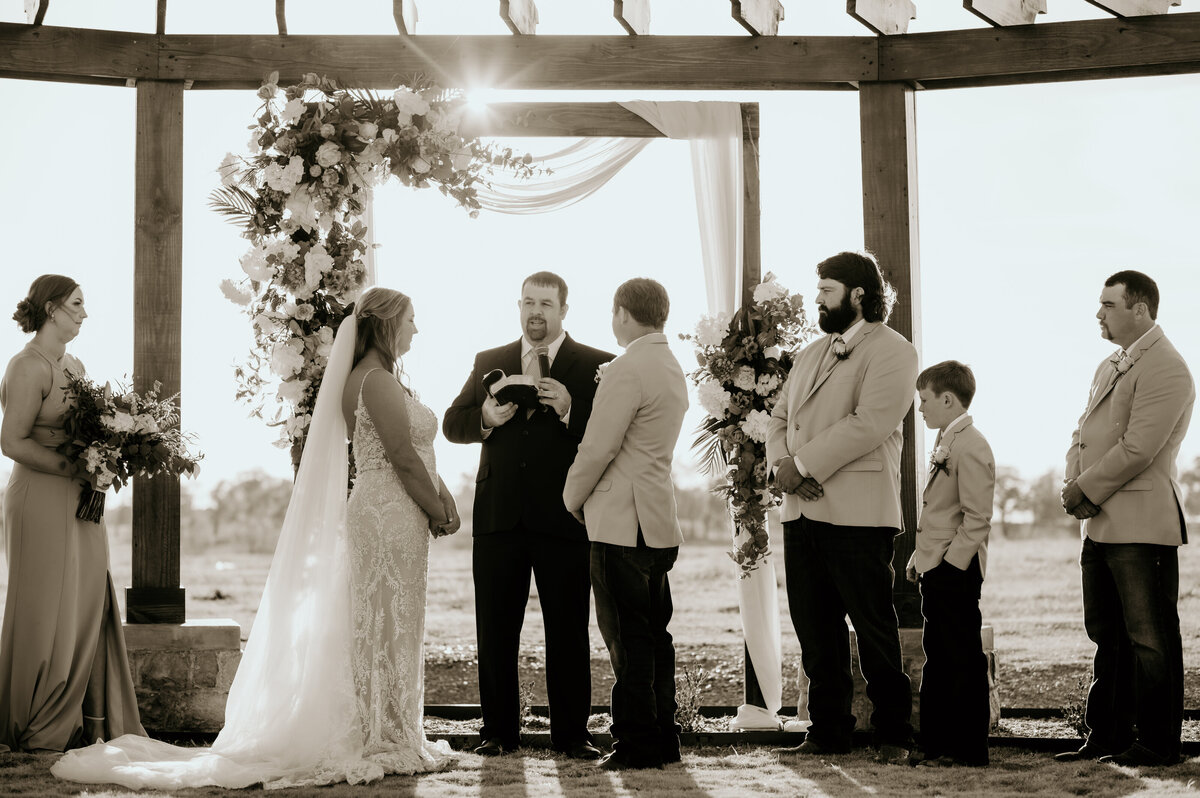 bride and groom standing together at the alter together with their bridal party on either side as the sun sets behind them