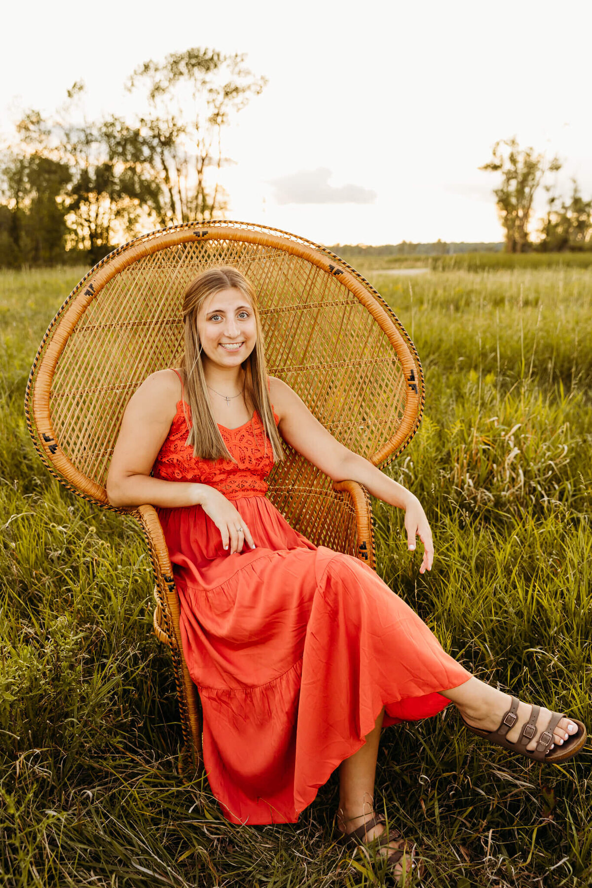 beautiful senior girl in an orange dress sitting in a peacock chair by Ashley Kalbus