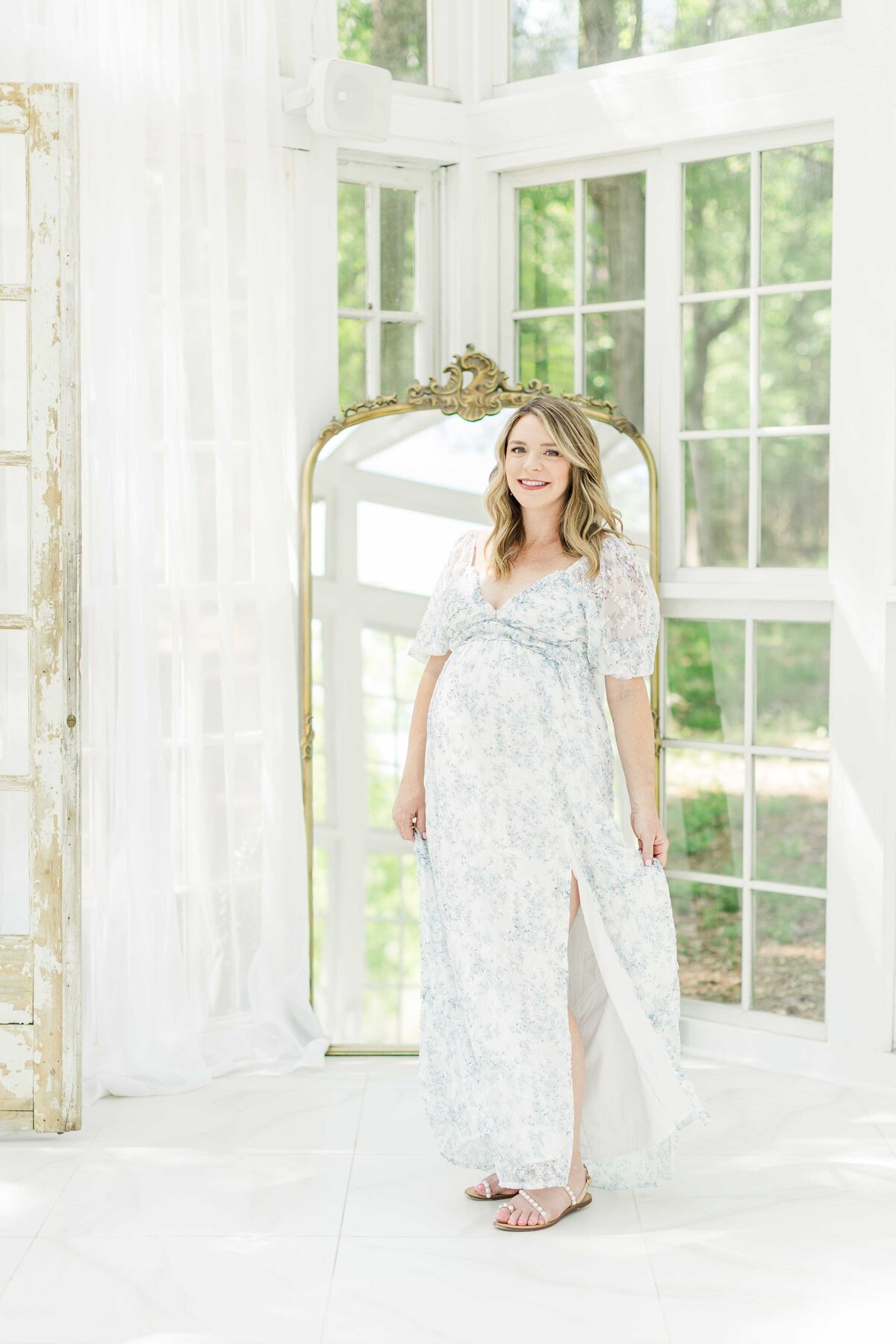 mom smiles in front of glass mirror for maternity photo session