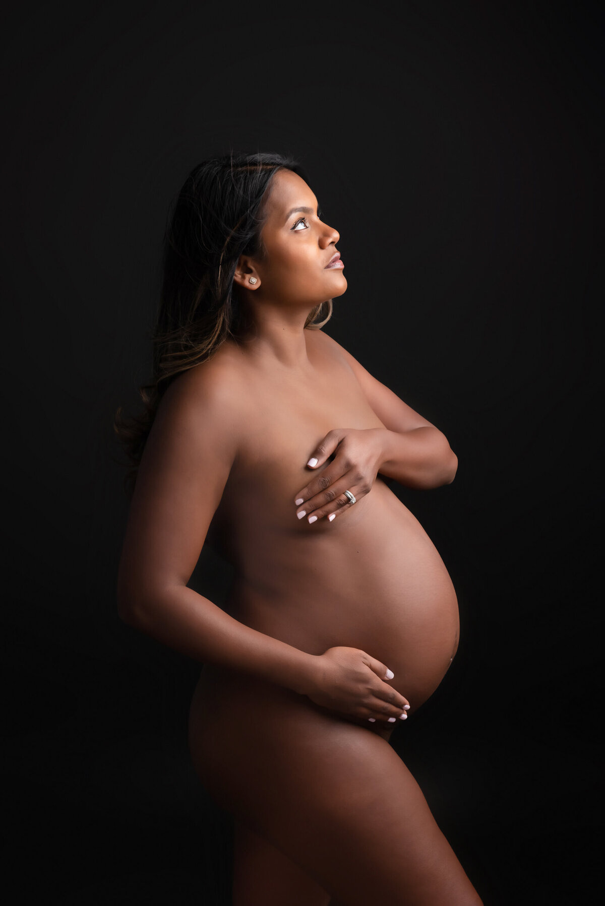 Black pregnant woman in front of a black background for her studio maternity photography session in Burlington, ON