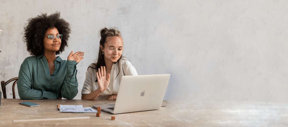 two women sitting at laptop and waving at a virtual meeting