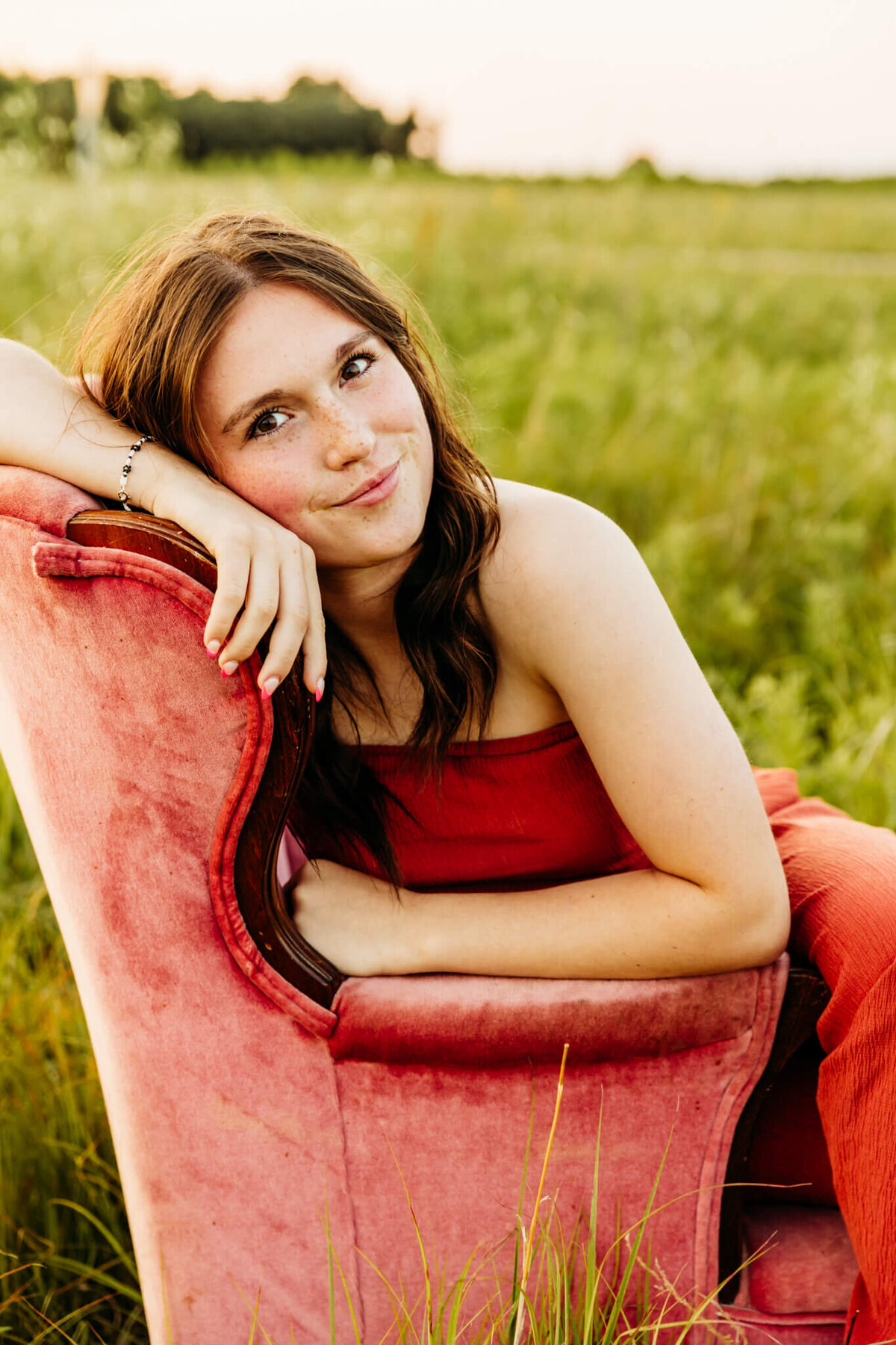 girl in an orange jumpsuit resting head on back of chair and glancing over