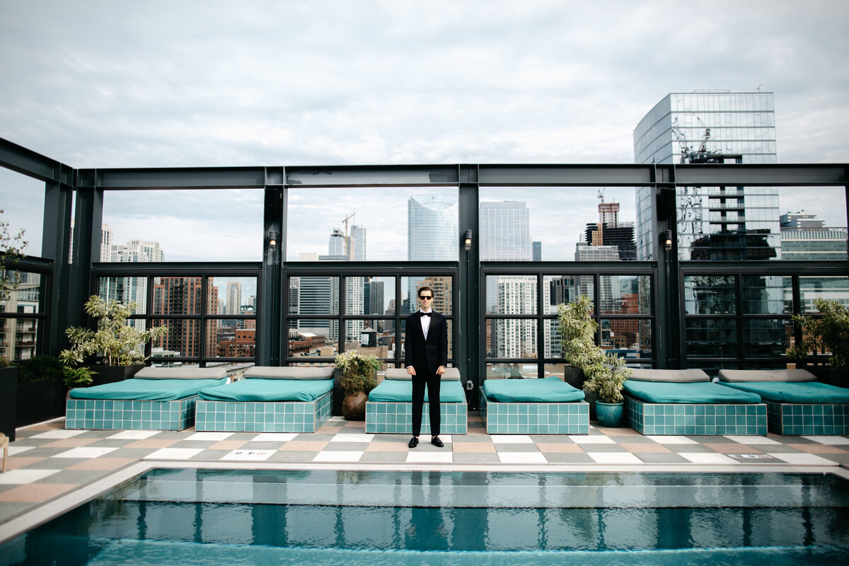 Wide angle image of groom standing on rooftop pool of Chicago hotel for first look