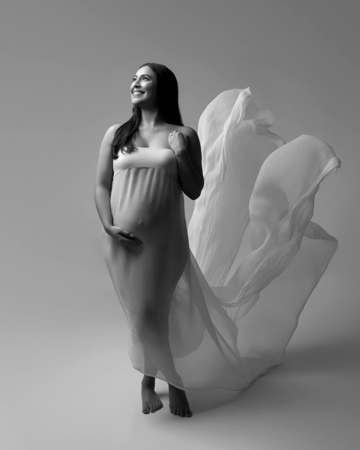 white silk fabric dress flying behind pregnant woman during maternity photoshoot