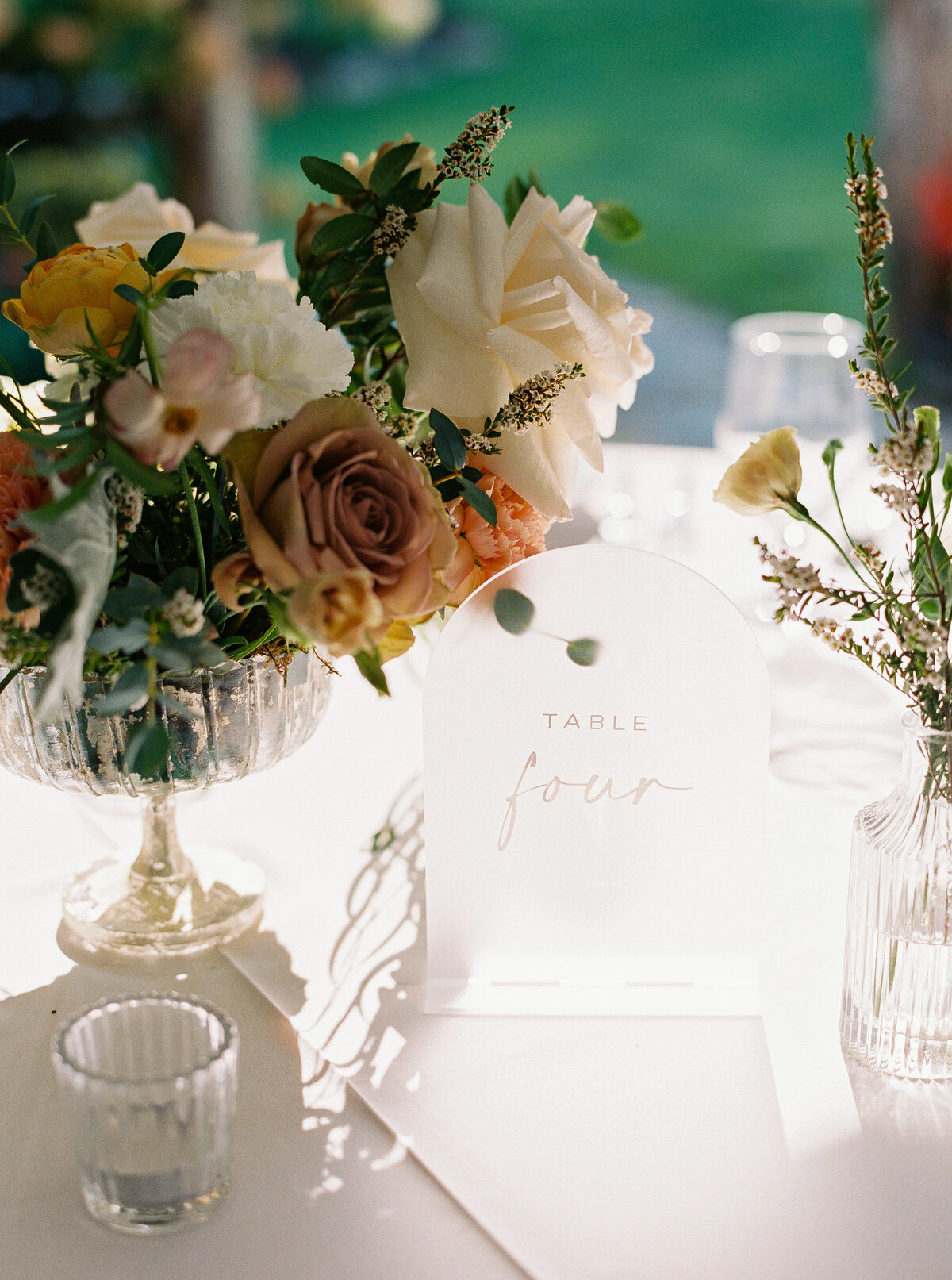 Acrylic table number beside a footed floral centerpiece with neutral and blush roses and greenery, styled on a reception table at Castle Ladyhawke

