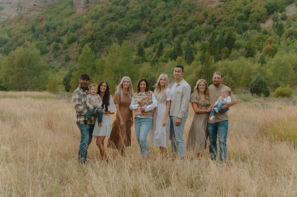 A large family consisting of 8 adults and 3 children all pose next to each other for a family portrait. They're standing in a tall grass field near Idaho Falls.