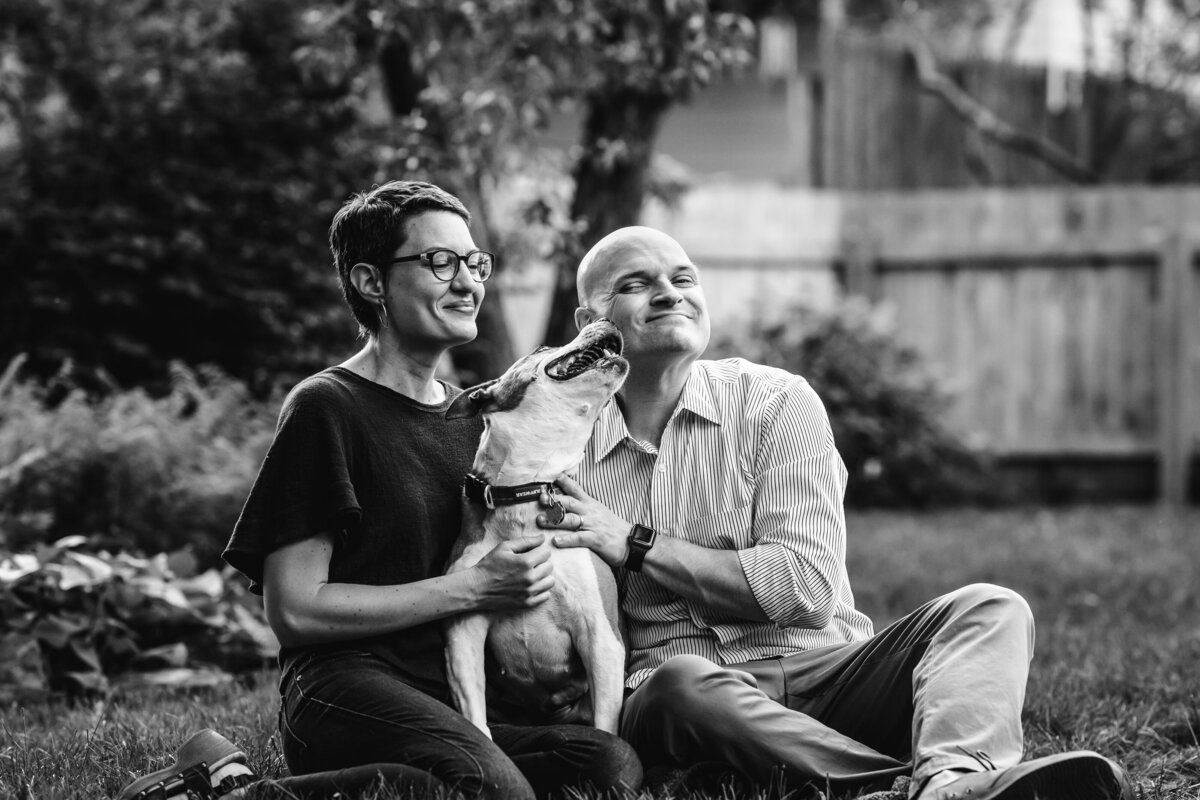 Man and woman sitting in the grass getting kissed by their dog Burlington Vermont Photographer