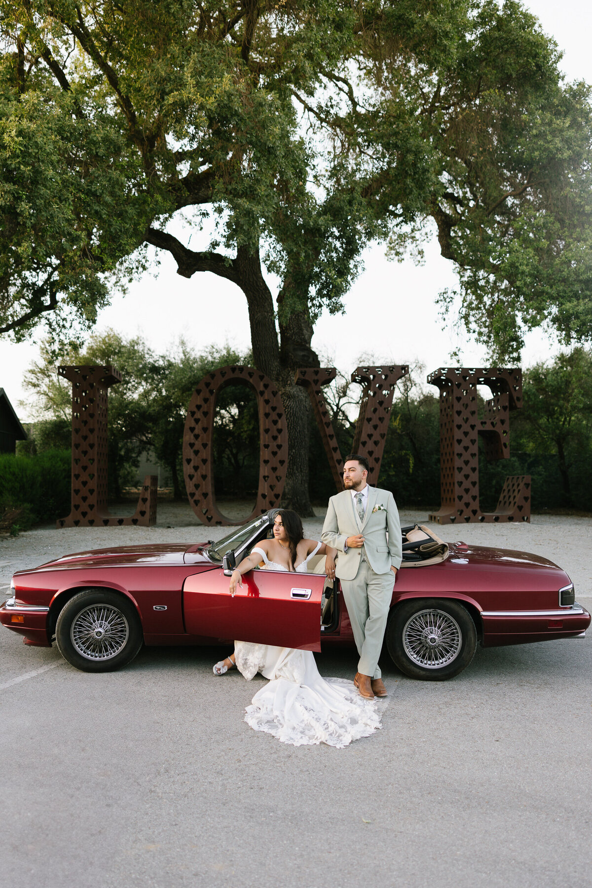 Couple on wedding day in a classic red Jaguar in from of a a Love sign at MoHi Winery  