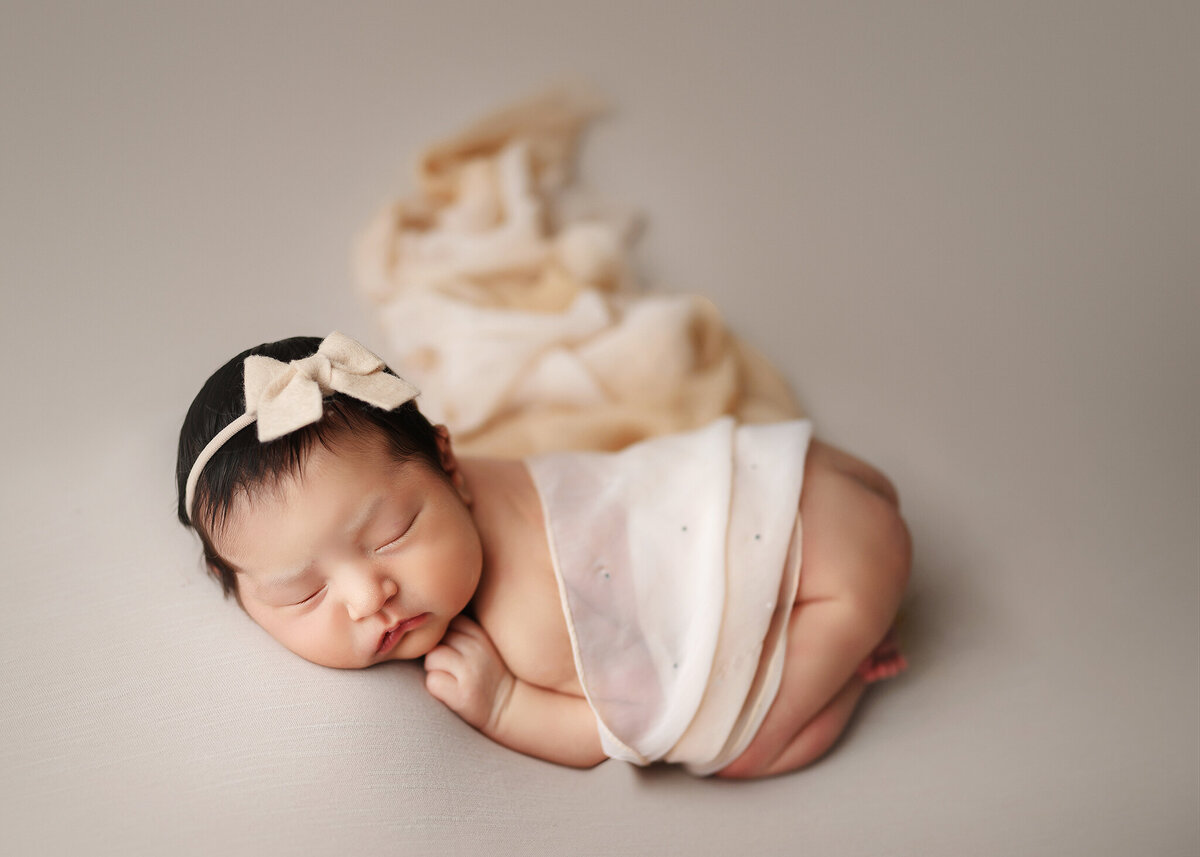 sleeping baby girl wrapped in silky scarf wearing a bow neutral tan tones