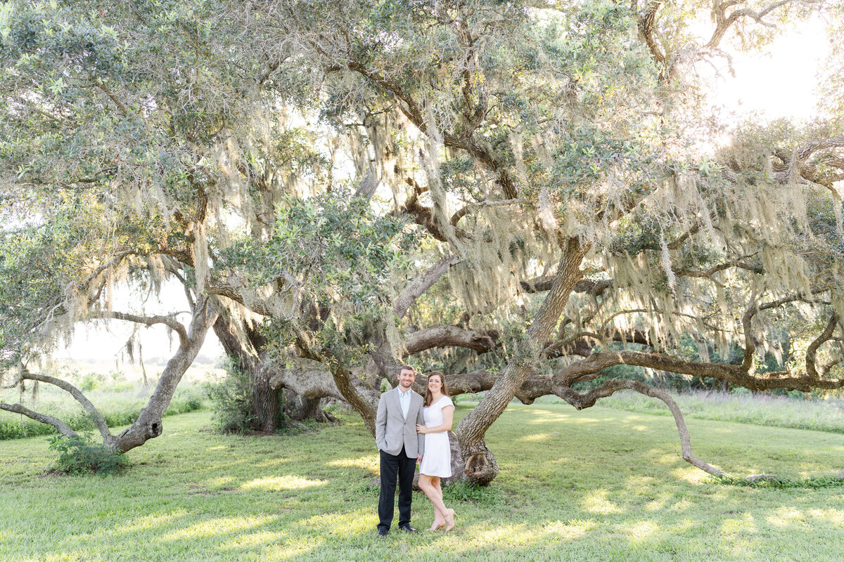 Future bride and groom smiling at camera under giant oak tree for engagement session at Brazos Bend State Park