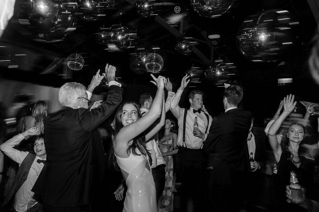 The bride and guests raise their hands in celebration while dancing under a canopy of hanging mirror balls.