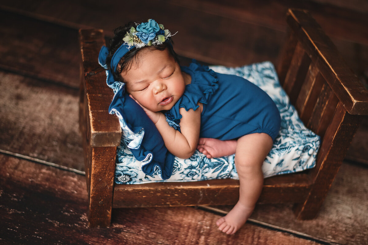 Baby girl dressed in blue sleeping on a wood bed prop at her photography session.