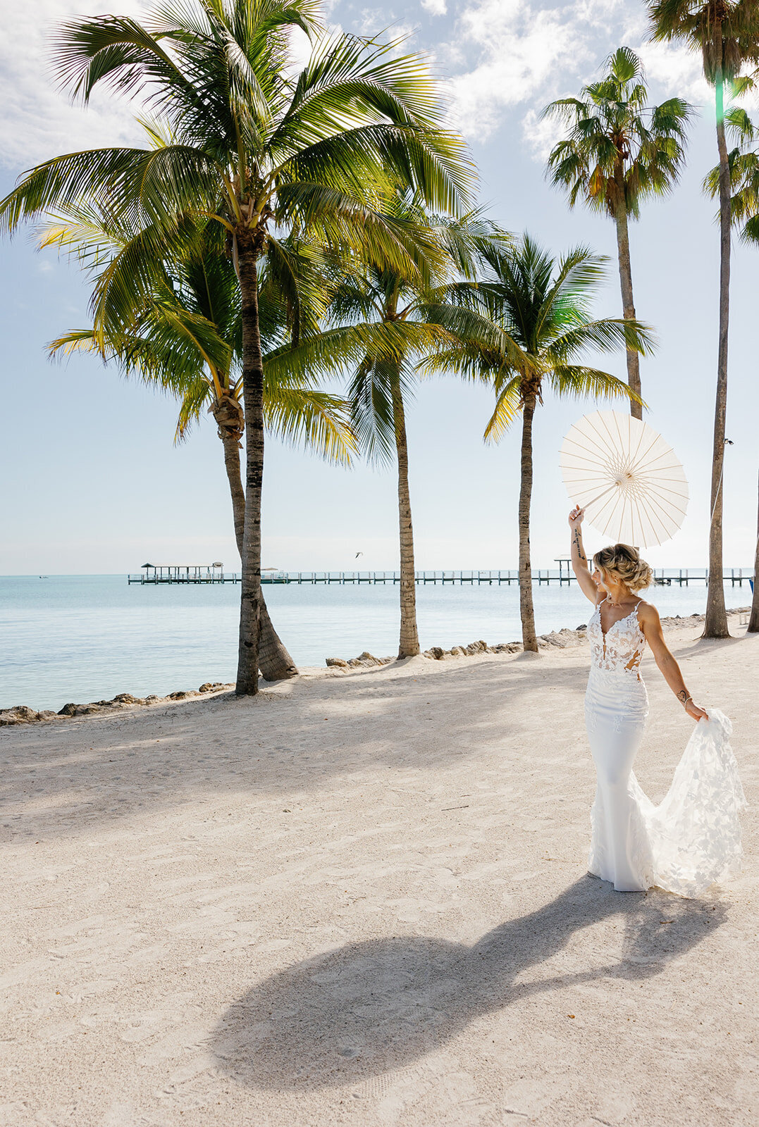 Ashley joyfully spins while holding a lace parasol, with the ocean and palm trees in the background.