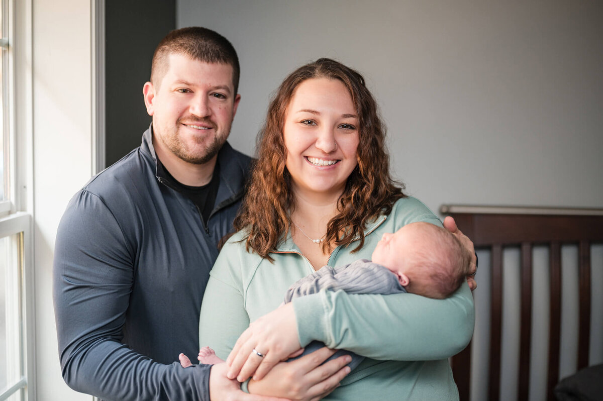 parents holding newborn by a window