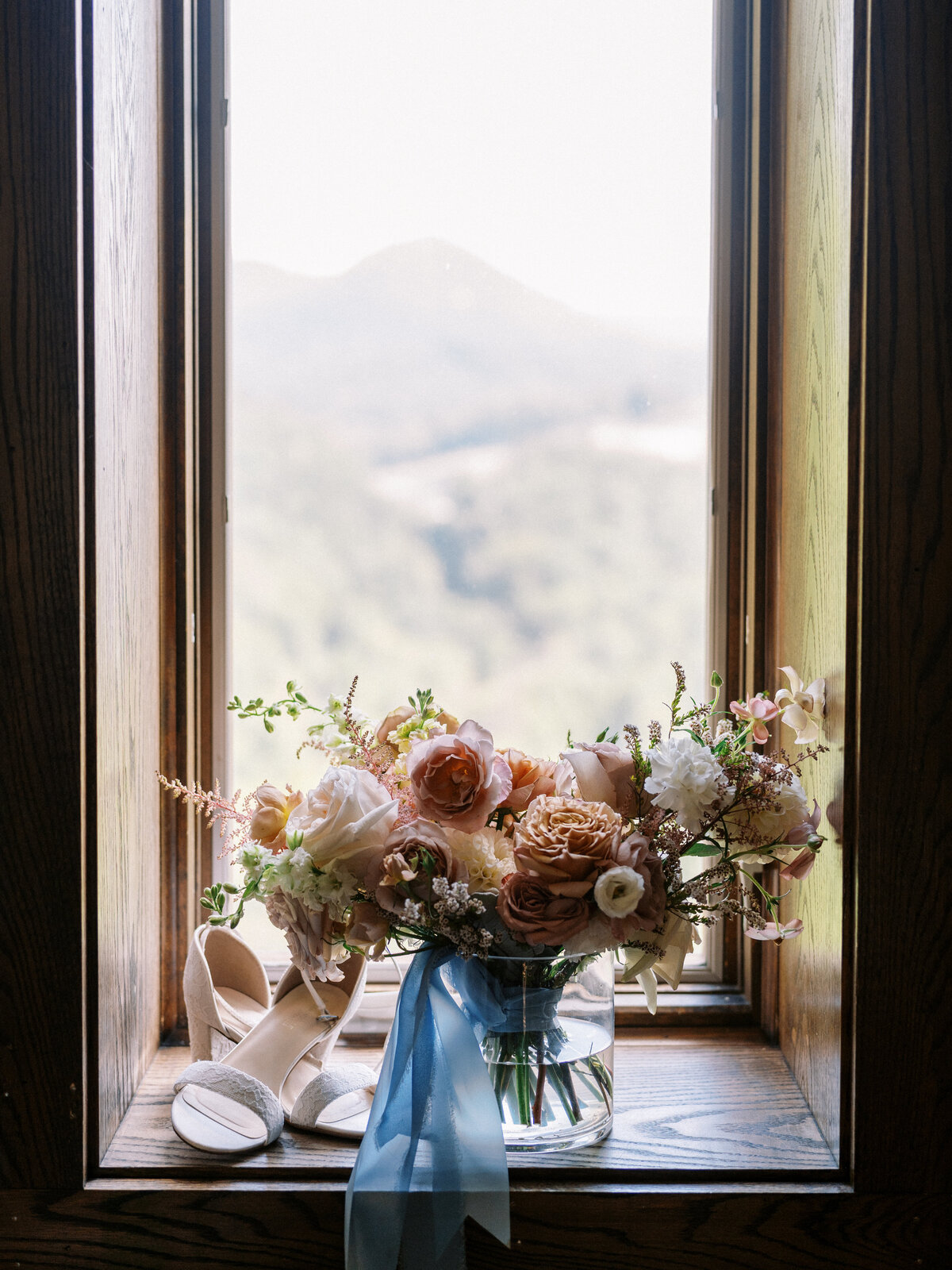 Bridal bouquet and wedding shoes displayed on a window ledge with soft mountain views at Castle Ladyhawke in North Carolina.