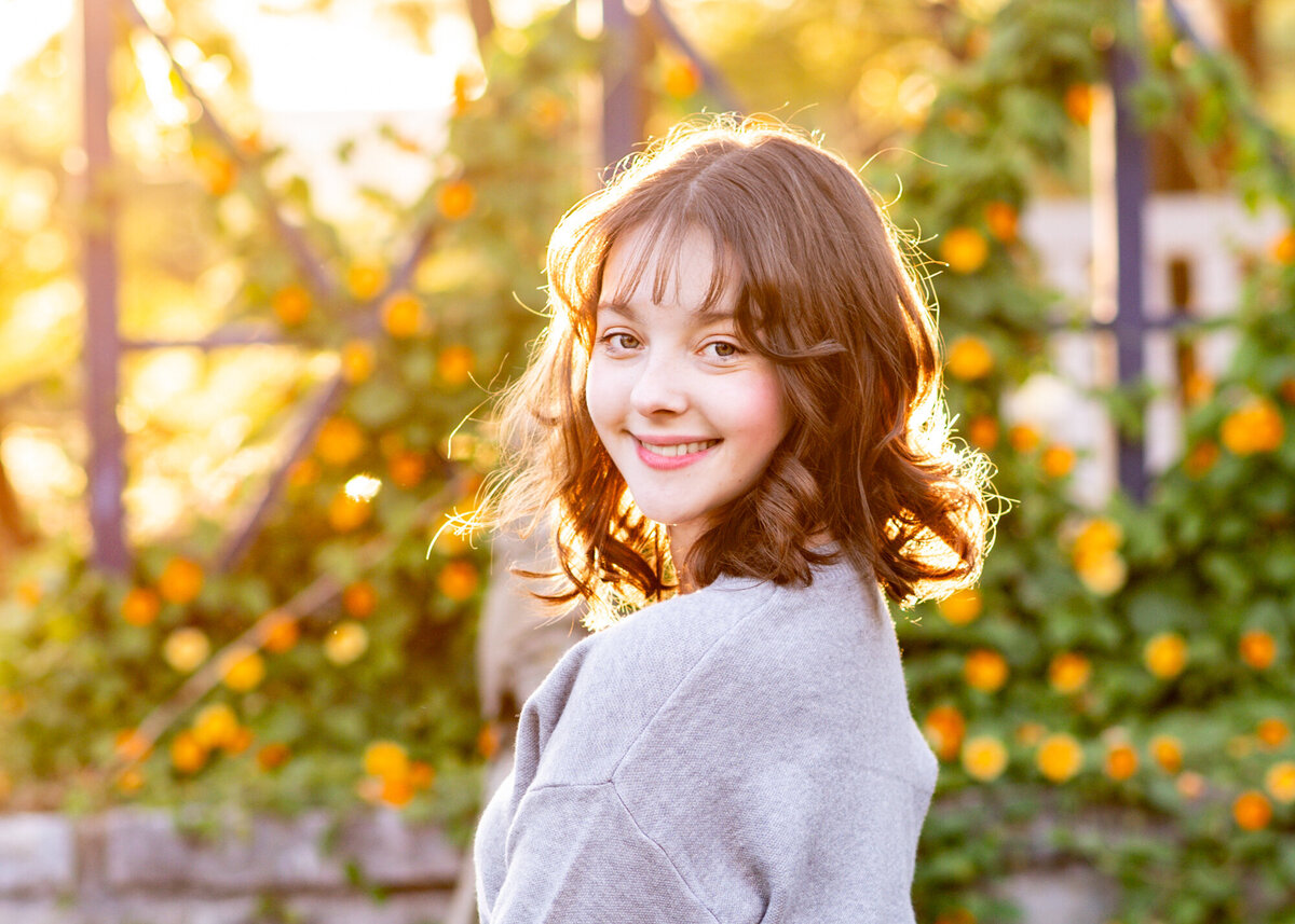 Senior portrait of a pretty girl wearing a gray sweater taken at a park during golden hour